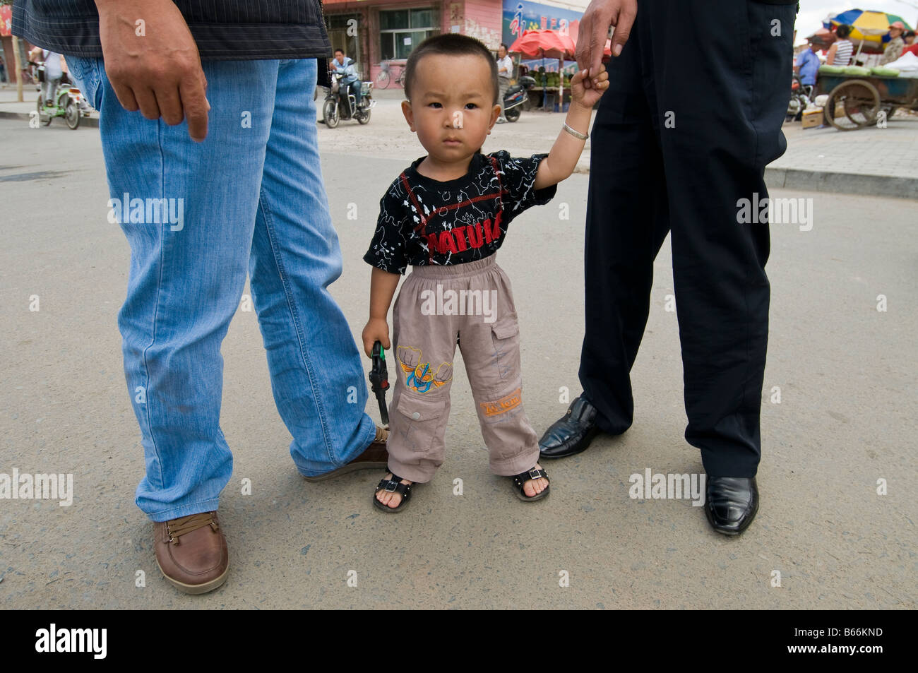 Ragazzo con pistola giocattolo in strada con adulti Xiwuzhumuqinqi Inner Mongolia Cina Foto Stock