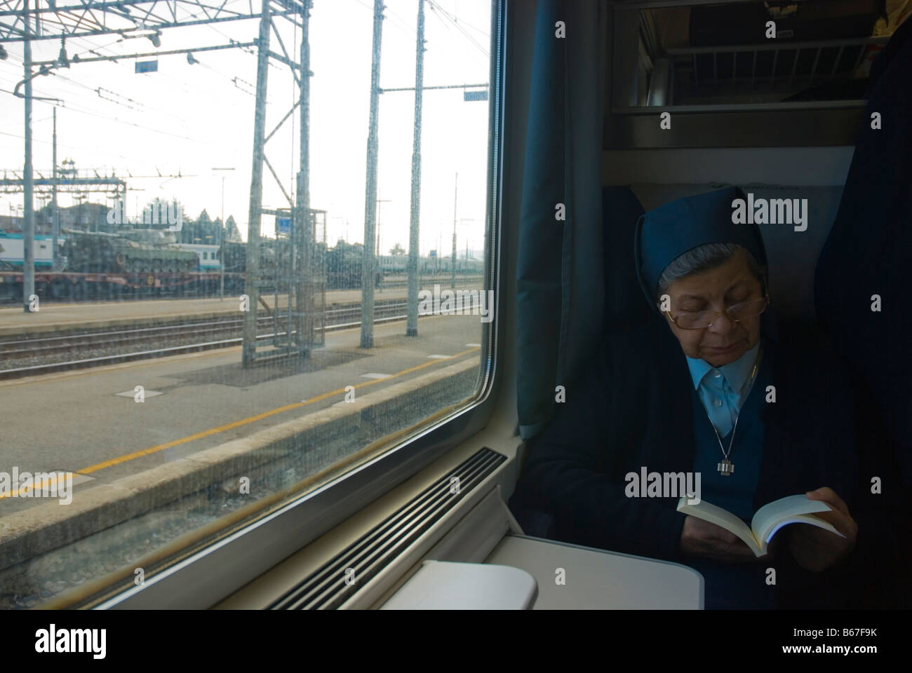 Nun lettura su un treno a Chiusi stazione ferroviaria con i serbatoi e le altre attrezzature militari al di fuori in Italia Europa Foto Stock