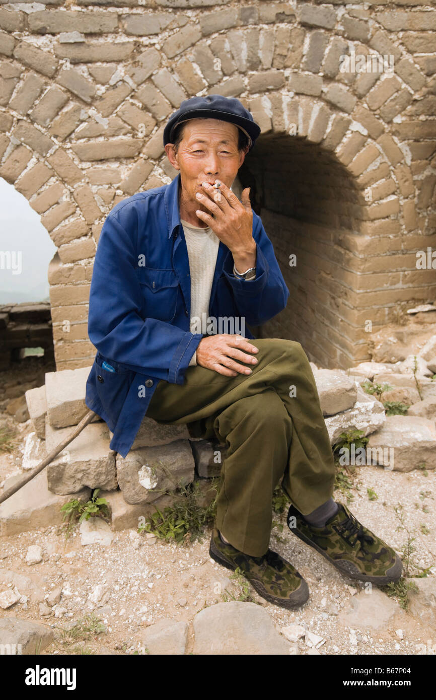 Uomo senior di fumare su una parete, la Grande Muraglia Cinese a Pechino, Cina Foto Stock