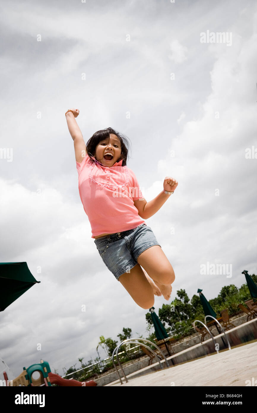 Sud-est asiatico ragazza adolescente così felice saltando da Hotel Ristorante a lato piscina mentre è in vacanza Foto Stock