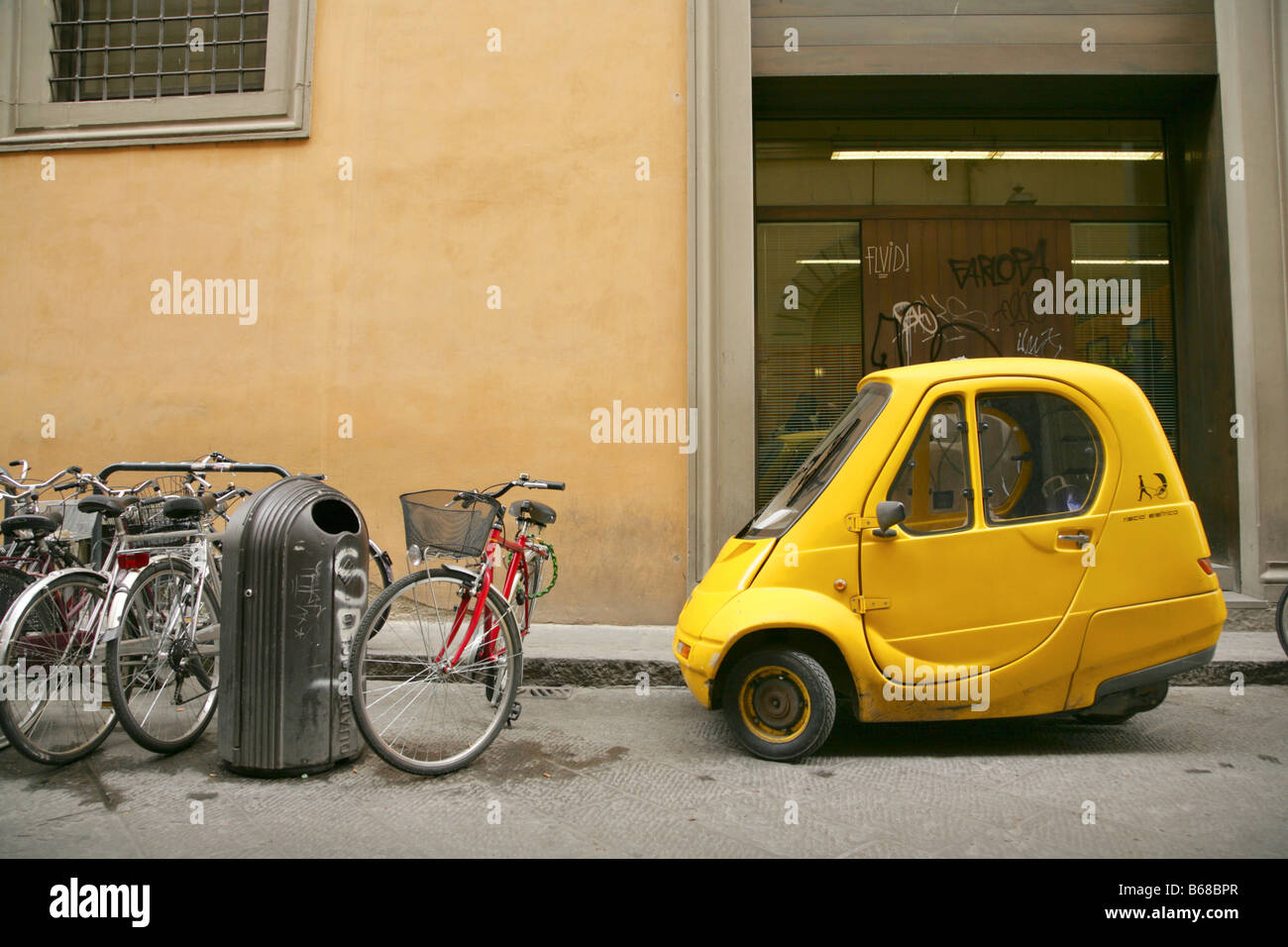 Biciclette e piccolo giallo a una sola persona di electric Pasquali Riscio auto parcheggiate in strada laterale, Firenze, Italia. Foto Stock