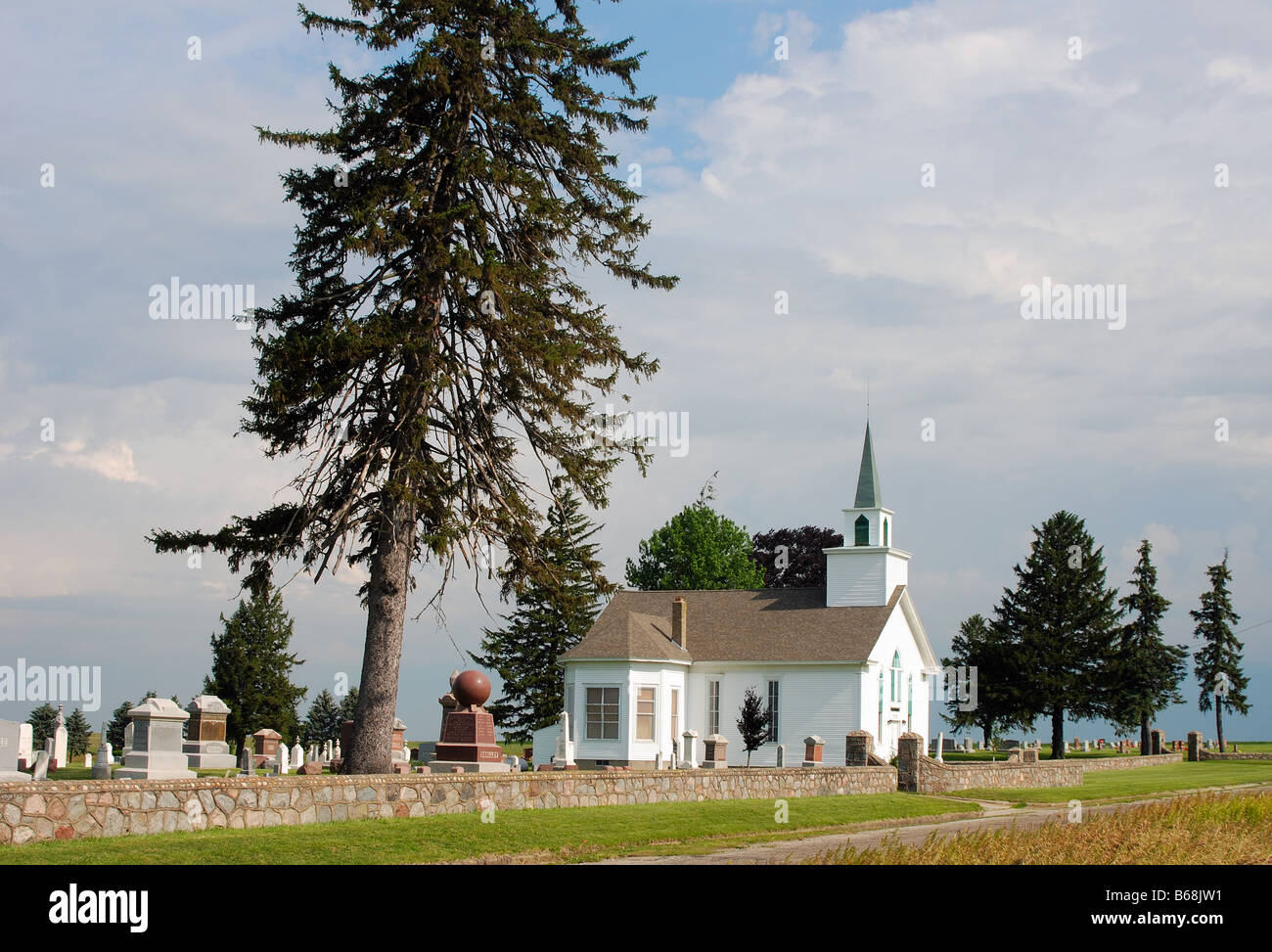 Piccolo paese bianco chiesa con una guglia verde accanto a un cimitero Foto Stock