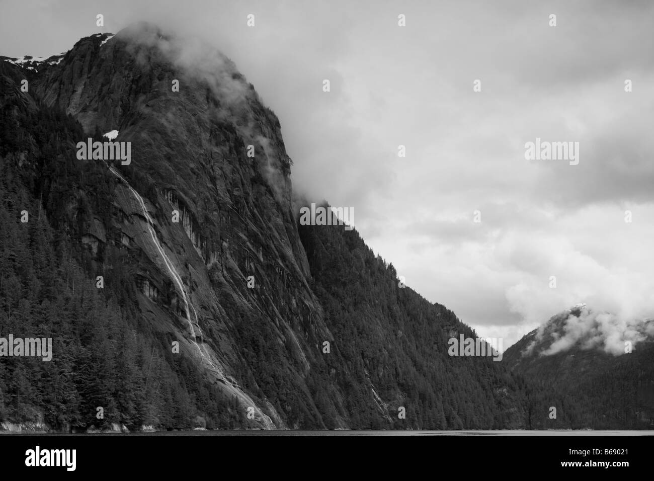 Stati Uniti d'America Alaska Misty Fjords National Monument nuvole swirl intorno ripida parete di roccia e cascata sopra Rudyerd Bay Foto Stock