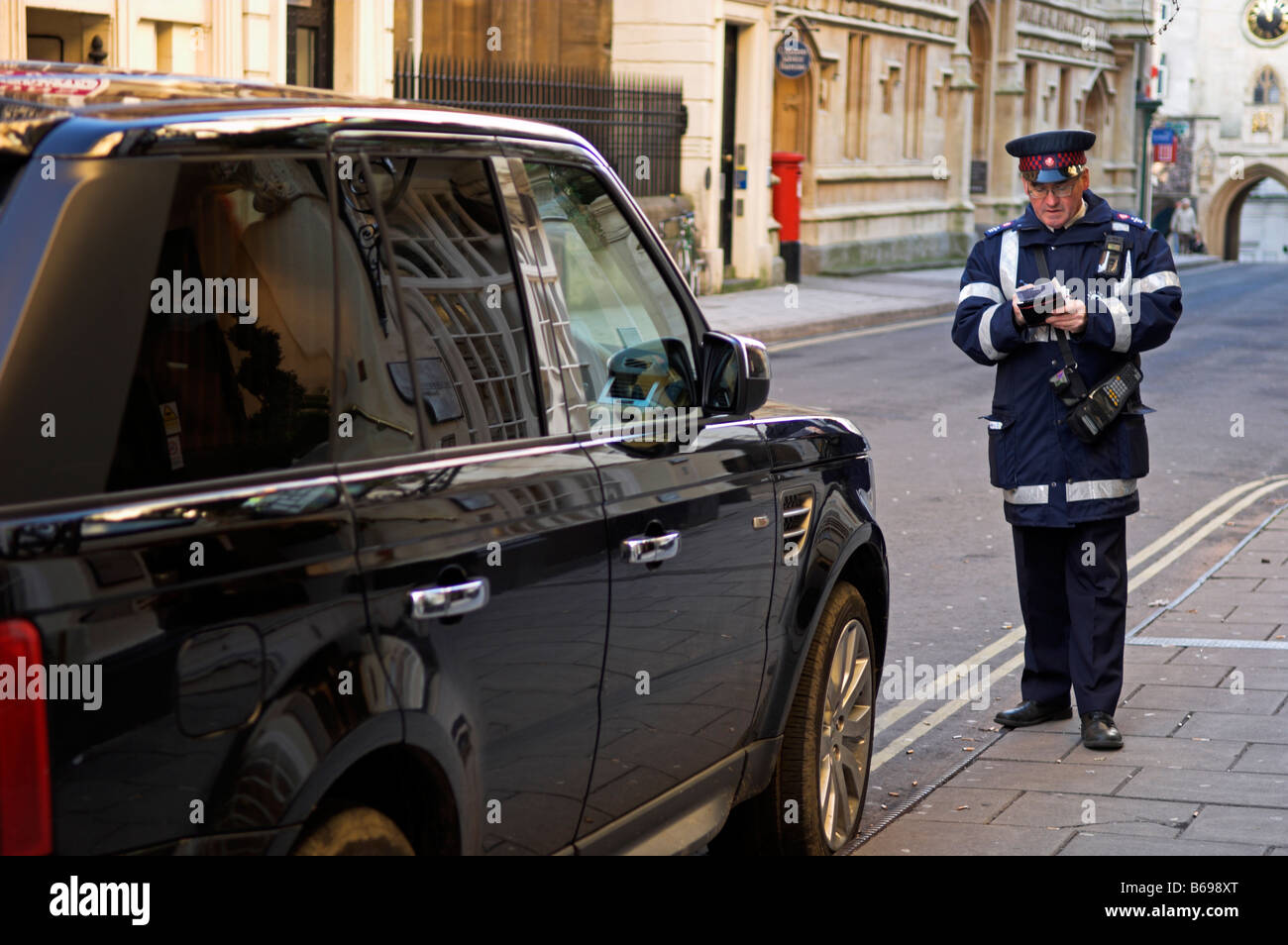 Vigile di emettere un biglietto di parcheggio su auto parcheggiate illegalmente sulle doppie linee gialle Foto Stock