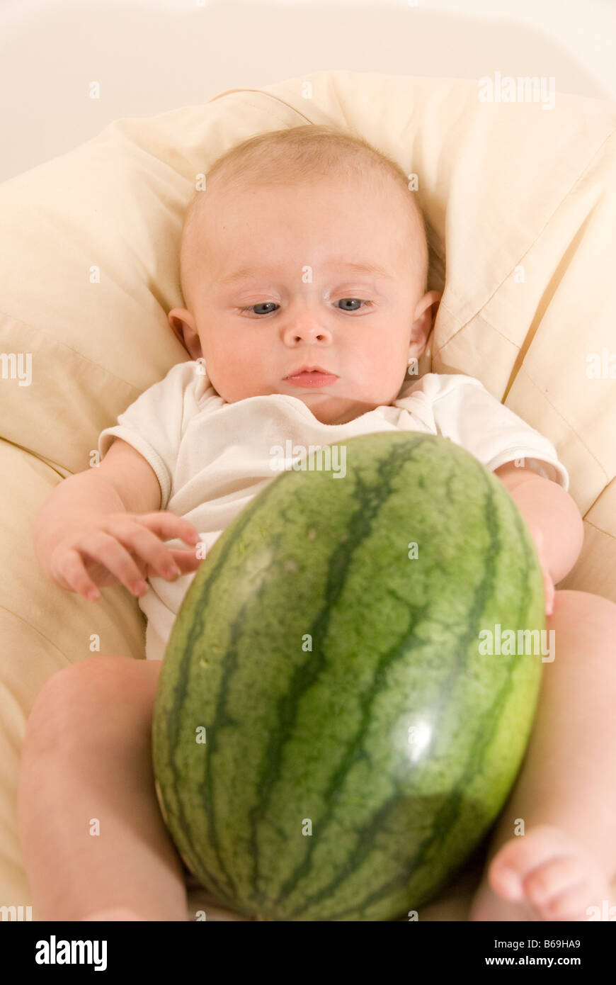 Bambino seduto in crema bianca Beanbag giocando con grande anguria verde Foto Stock