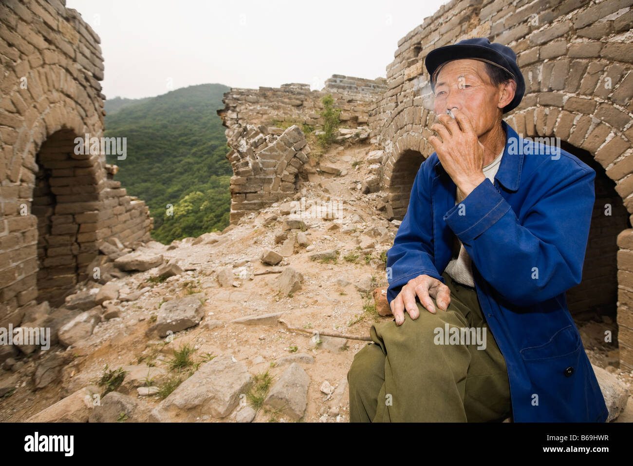 Uomo senior di fumare su una parete, la Grande Muraglia Cinese a Pechino, Cina Foto Stock