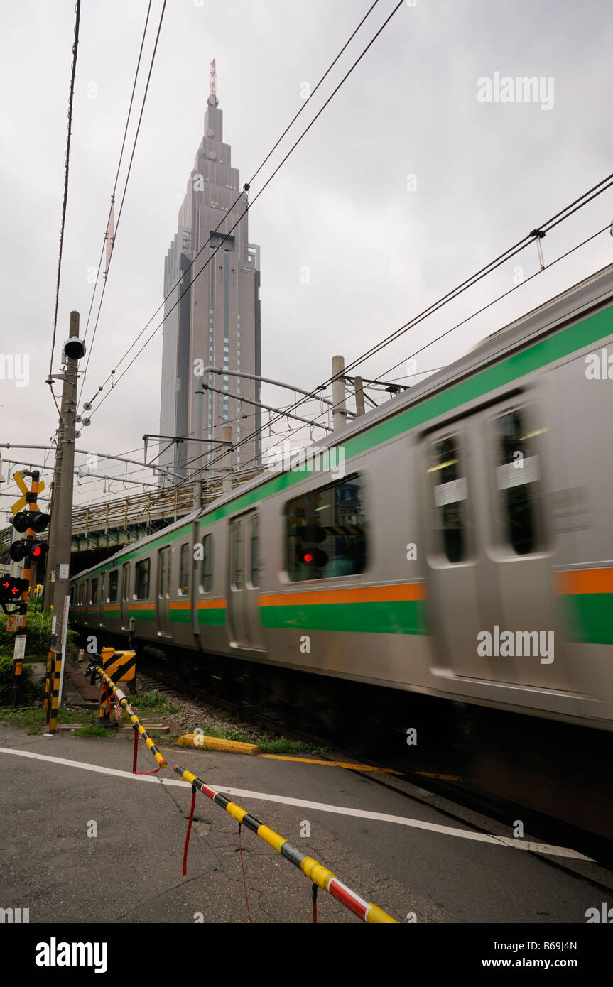 NTT DoCoMo Yoyogi edificio (fondo) e a un treno in movimento su una strada attraverso railroad crossing. Shinjuku. Tokyo. Il Giappone. Foto Stock