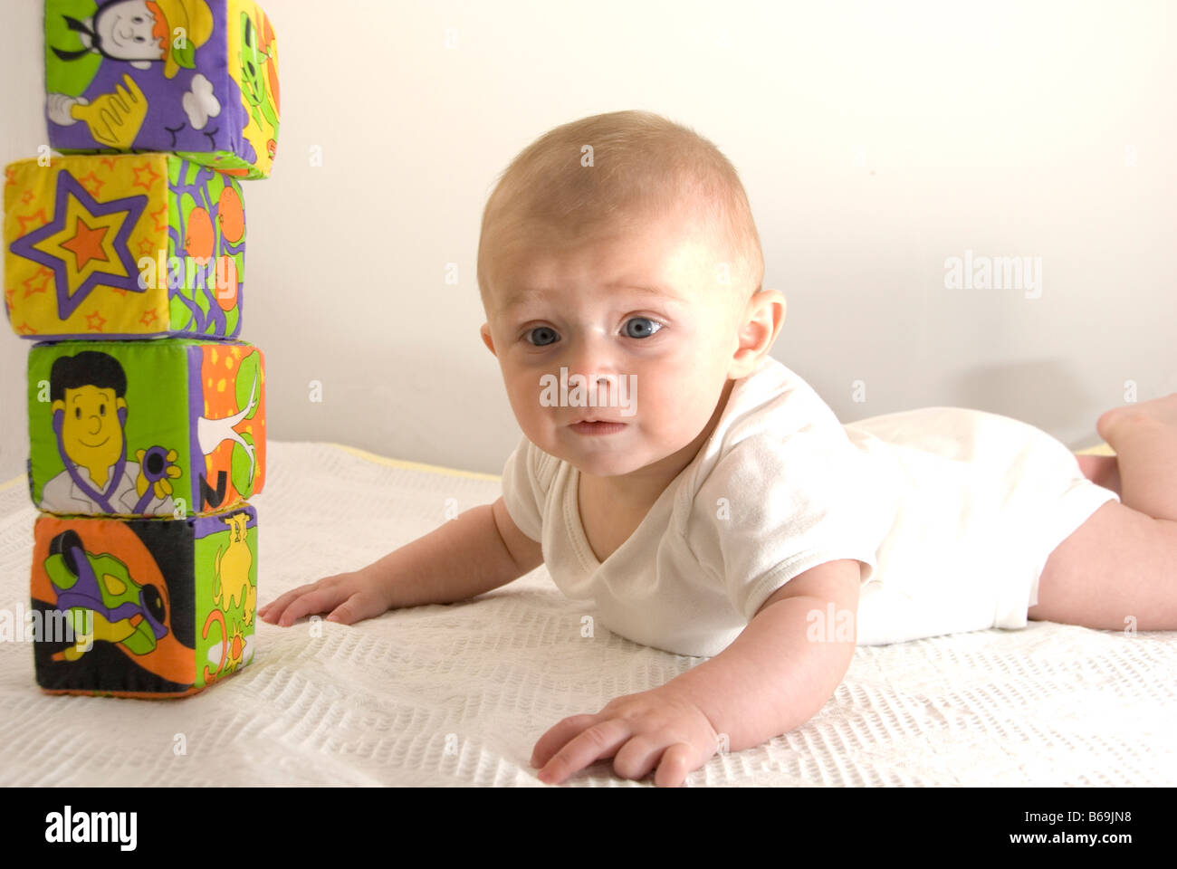 Baby Boy con pila di mattoni giocattolo guardando direttamente alla fotocamera con espressione perplessa tagliati su bianco Foto Stock