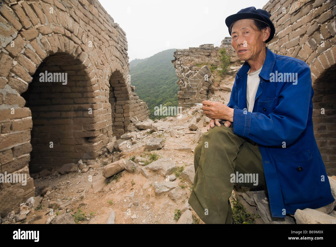 Ritratto di un anziano uomo seduto su una parete, la Grande Muraglia Cinese a Pechino, Cina Foto Stock