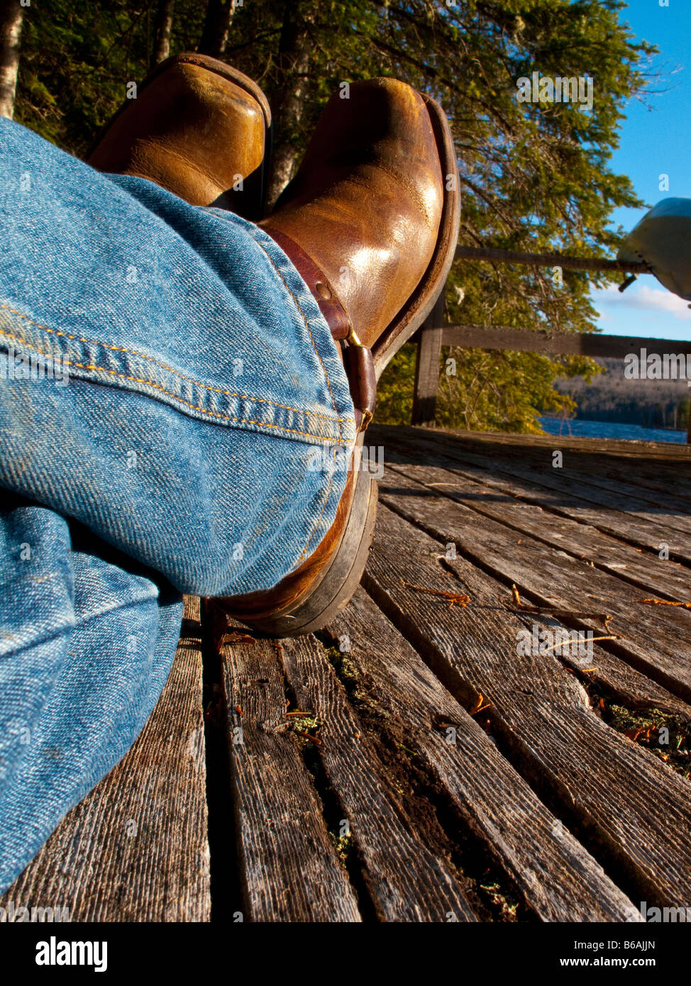 Stivali da cowboy e jeans blu di un uomo seduto sul vecchio dock con legno  stagionato Foto stock - Alamy