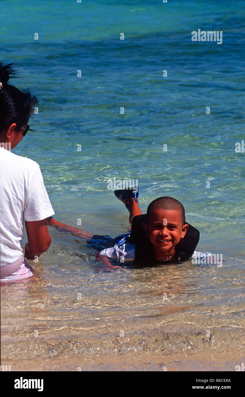Con sua madre accanto a lui, Little Boy in life jacket riproduce in modo sicuro nel Mar dei Caraibi. Foto Stock