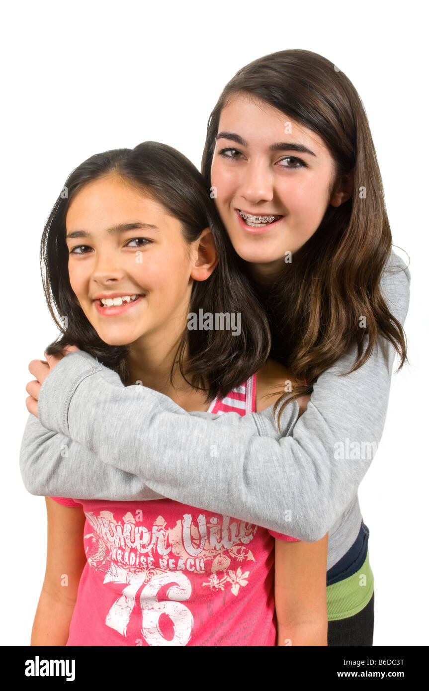 Chiudere verticale su ritratto di due sorelle adolescenti, la sorella maggiore dando la più giovane un abbraccio, contro uno sfondo bianco Foto Stock