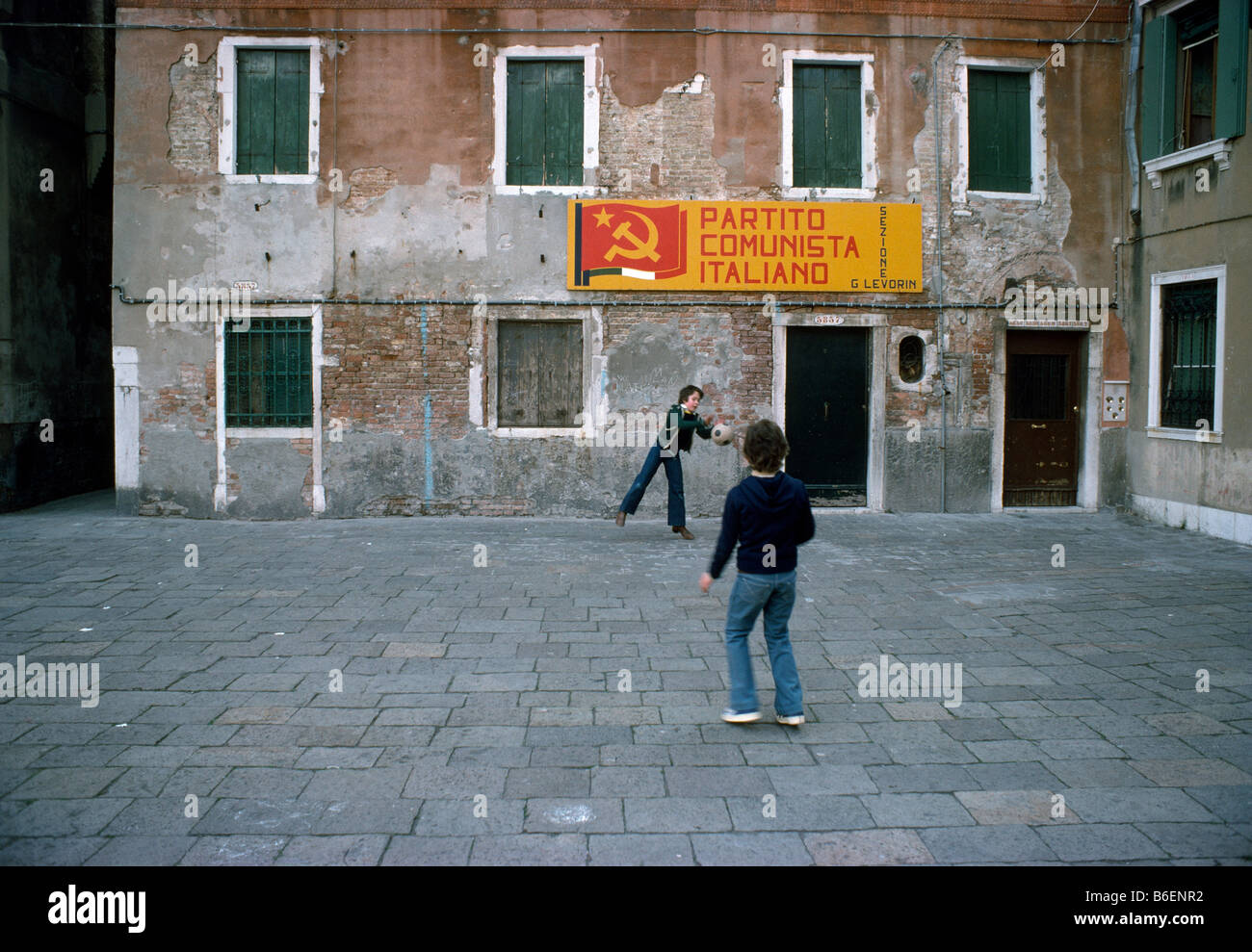 Due ragazzi giocare a calcio in un cortile di Venezia sotto un Partito comunista italiano (PCI) banner in aprile 1976. Foto Stock