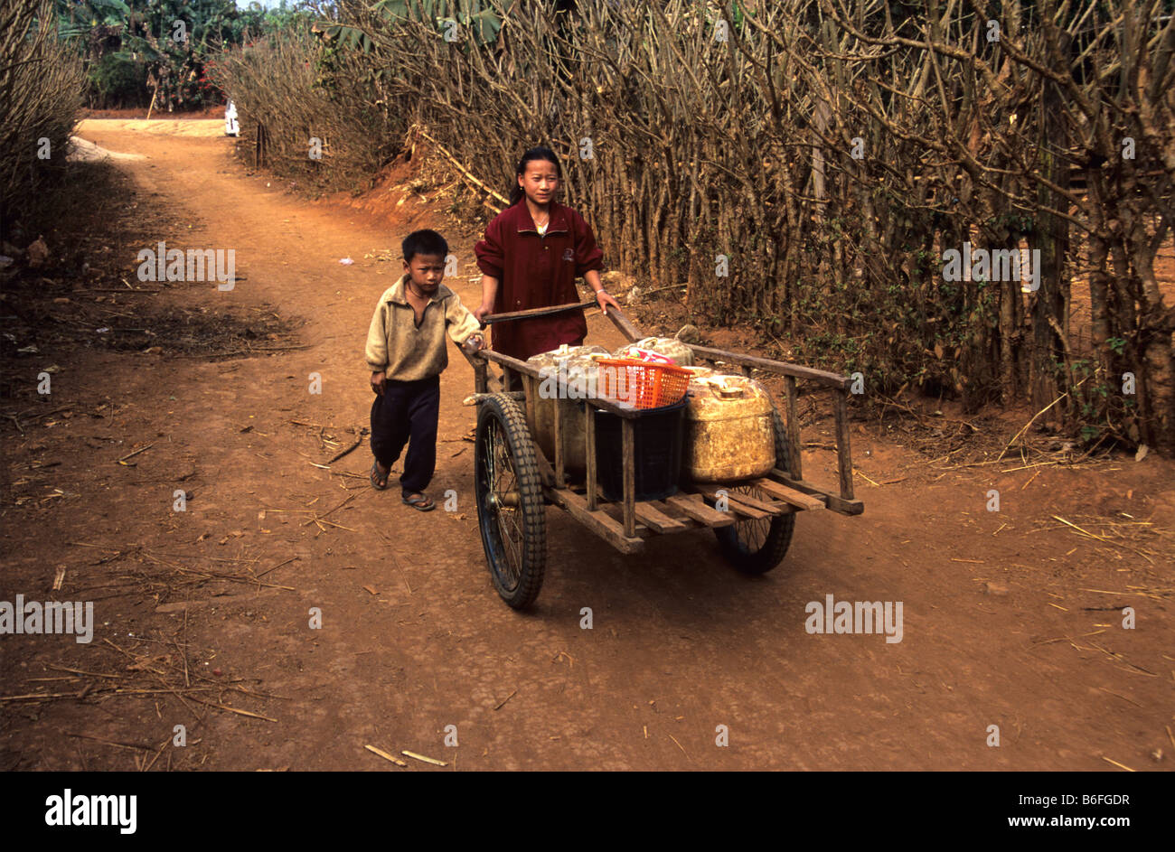 Una ragazza Hmong e suo fratello a spingere un carrello a mano lungo la corsia polveroso di un villaggio hmong vicino a Phonsavan, Xieng Khuang Prov. Laos Foto Stock
