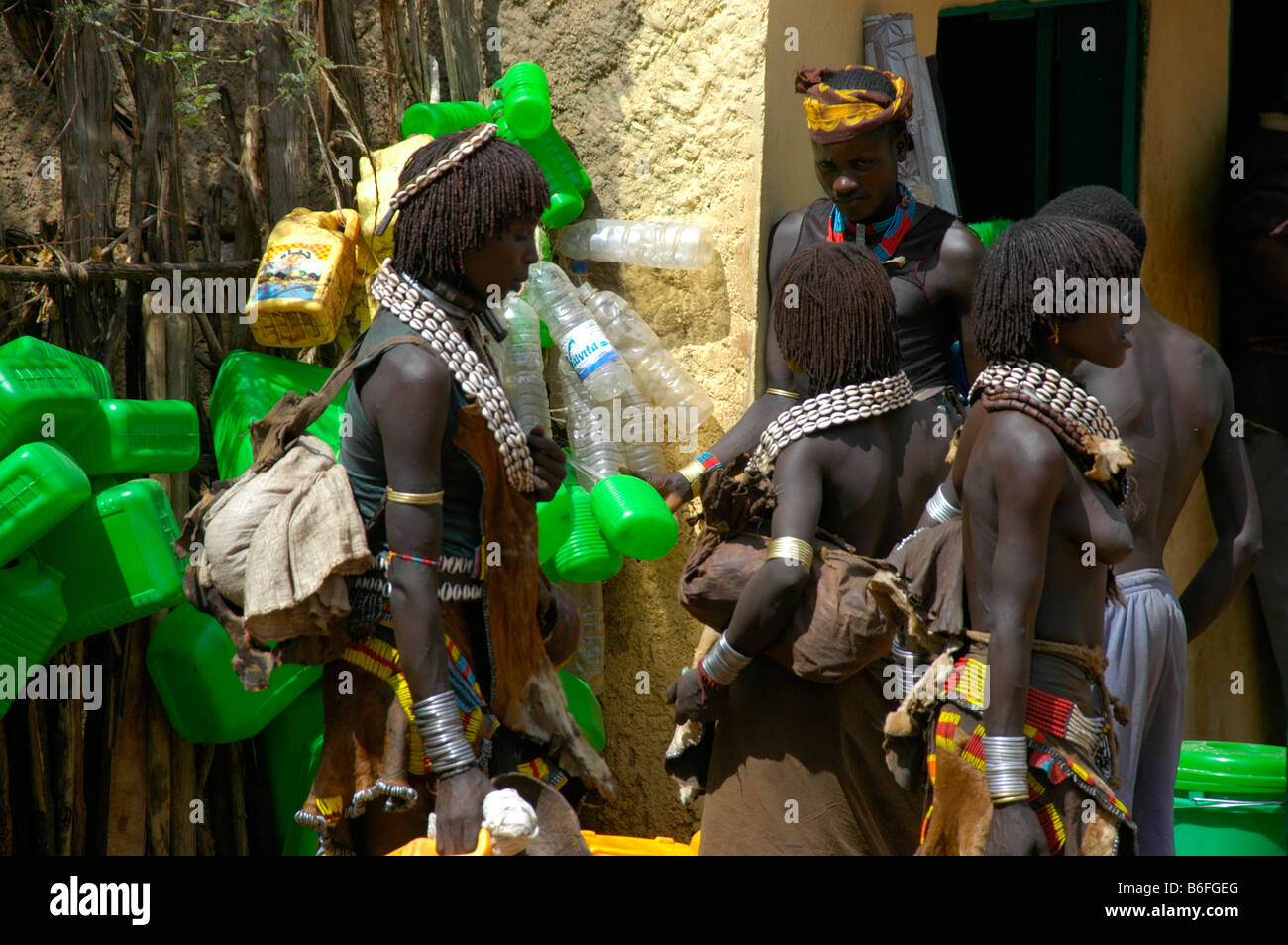 Nero scuoiati Hamar persone con il bianco kauri cozza collane di fronte verde barattoli di plastica, mercato di Dimeka, Etiopia, un Foto Stock