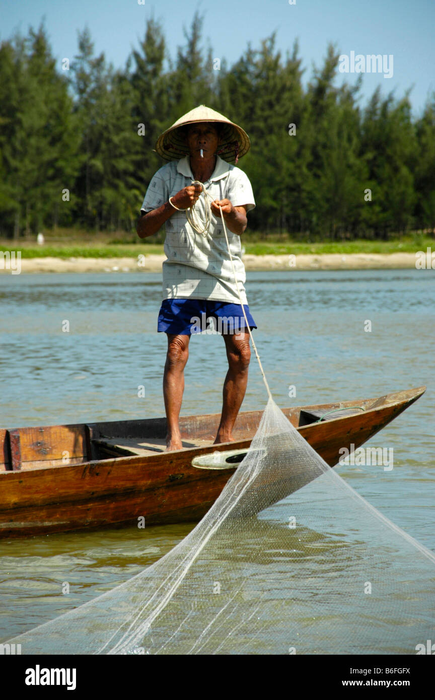 Pescatore con conformata a cono hat il recupero del net, fumare una sigaretta, Hoi An, Vietnam, sud-est asiatico Foto Stock