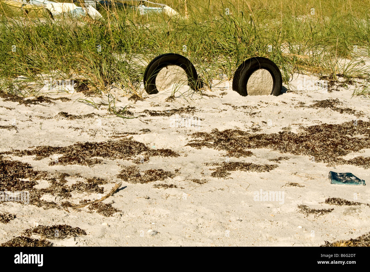 Due pneumatici di gomma riempita di sabbia sulla spiaggia tra l'erba e alghe marine Foto Stock