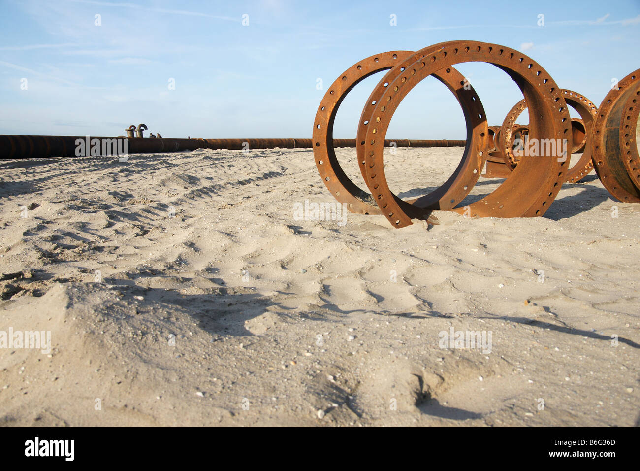 Rusty anelli circolari pipeline parti parzialmente sepolto nella spiaggia di sabbia con tubazione sull orizzonte sotto il cielo blu, Paesi Bassi Foto Stock