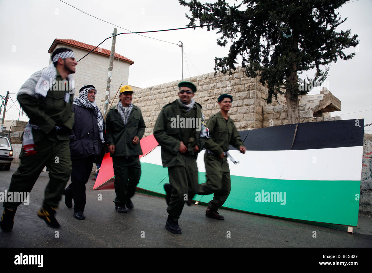 Palestinesi vestito come militanti del Fatah e in esecuzione passato una grande bandiera palestinese nel villaggio di Bilin in Cisgiordania. Foto Stock