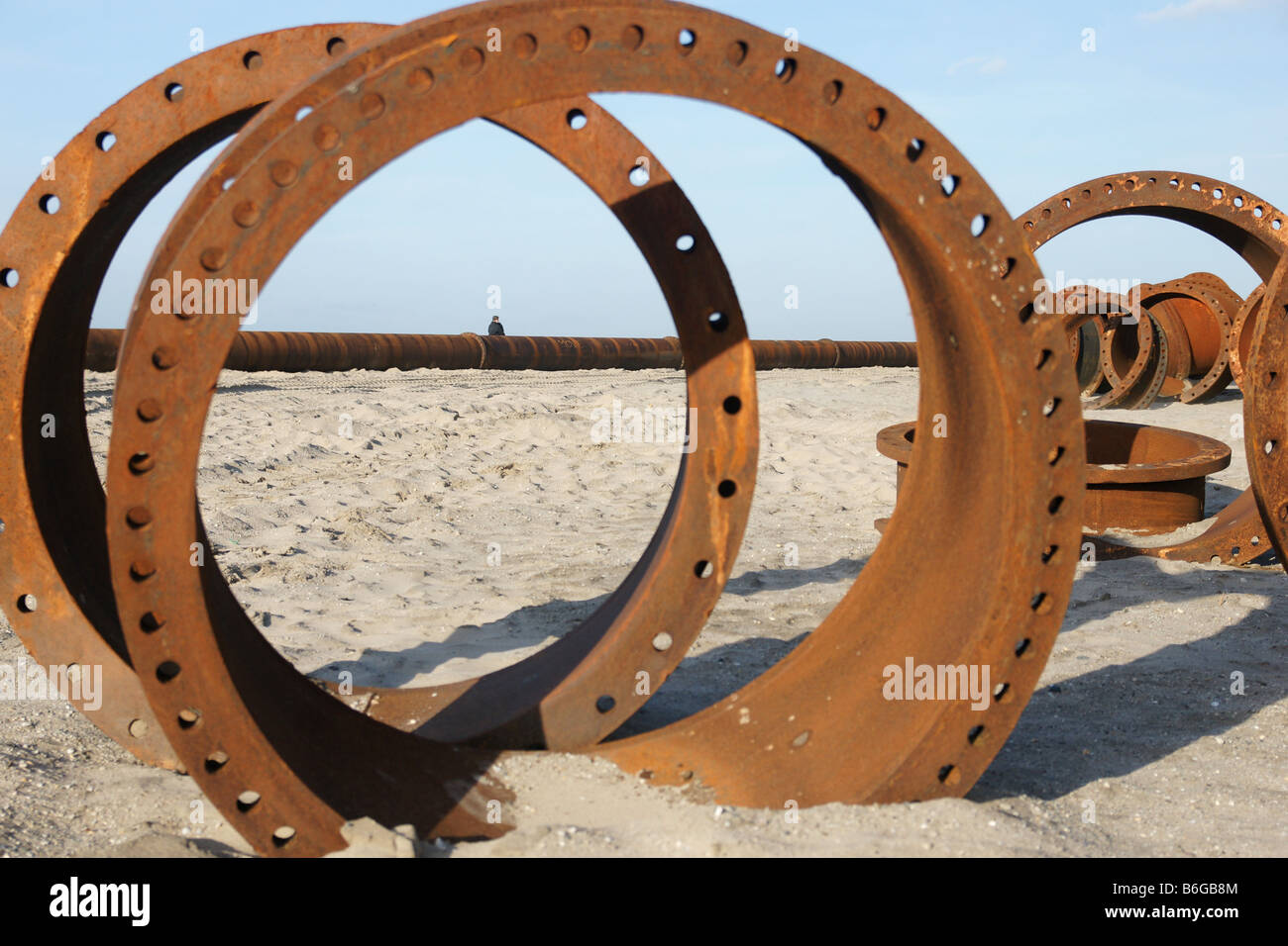 Rusty anelli circolari pipeline parti parzialmente sepolto nella spiaggia di sabbia con tubazione sull orizzonte sotto il cielo blu, Paesi Bassi Foto Stock