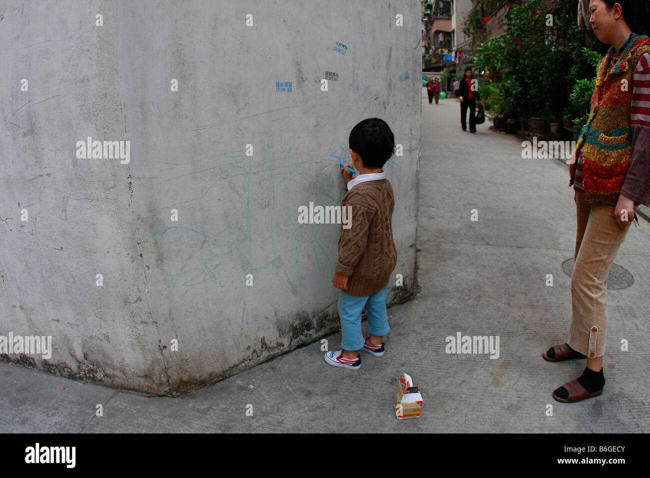 Giovani cinesi bambino prestando al di fuori del disegno di foto sulla parete Foto Stock