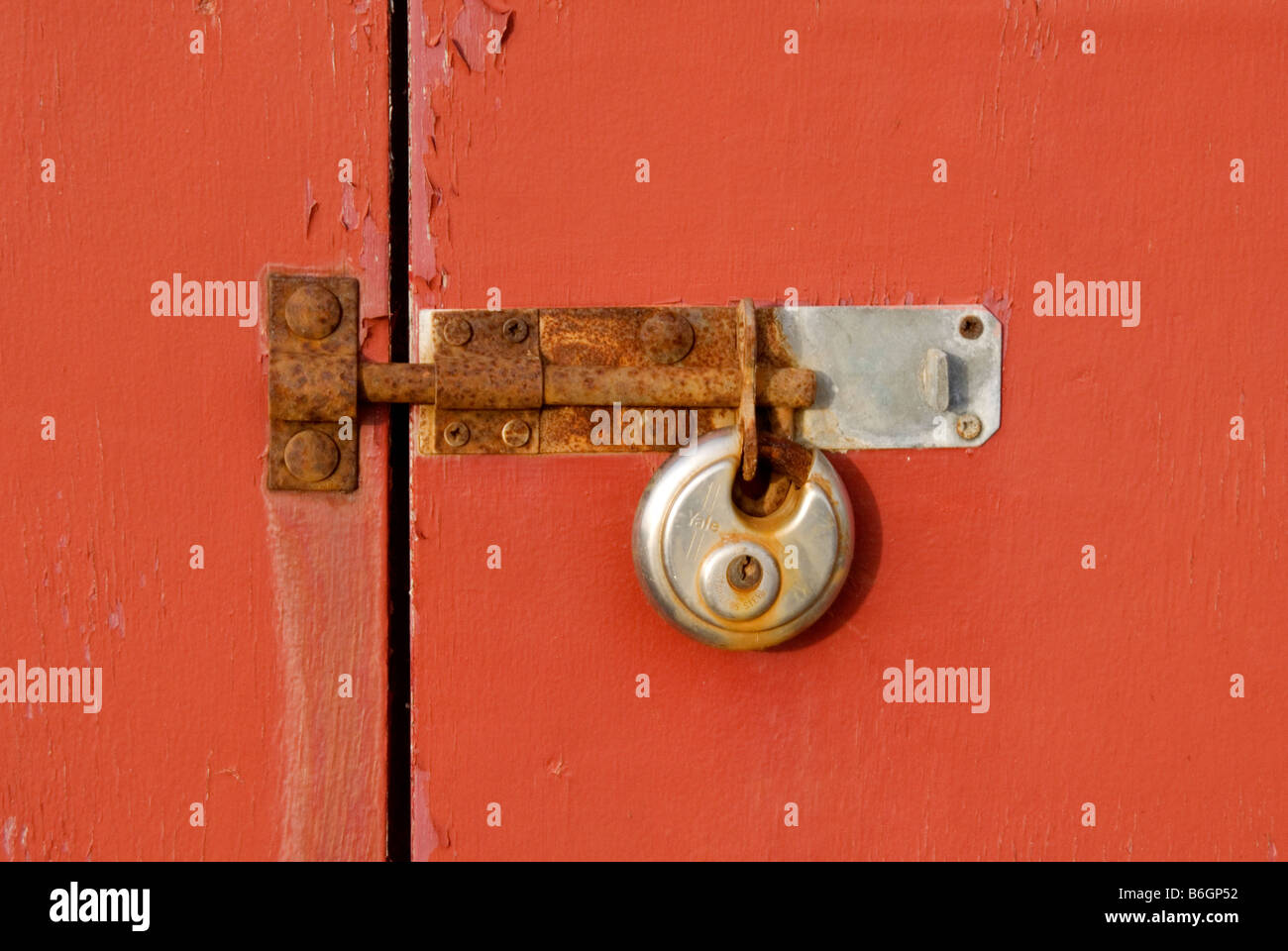 Un lucchetto arrugginito, bullone e cattura su rosso porta in legno con vernice scrostata off. Le porte di rosso riempire il telaio con il blocco centrato Foto Stock