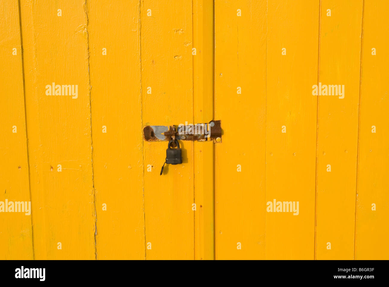 Un'immagine di un lucchetto arrugginito e cattura il colore giallo brillante con ante in legno, le porte gialle riempire il telaio Foto Stock