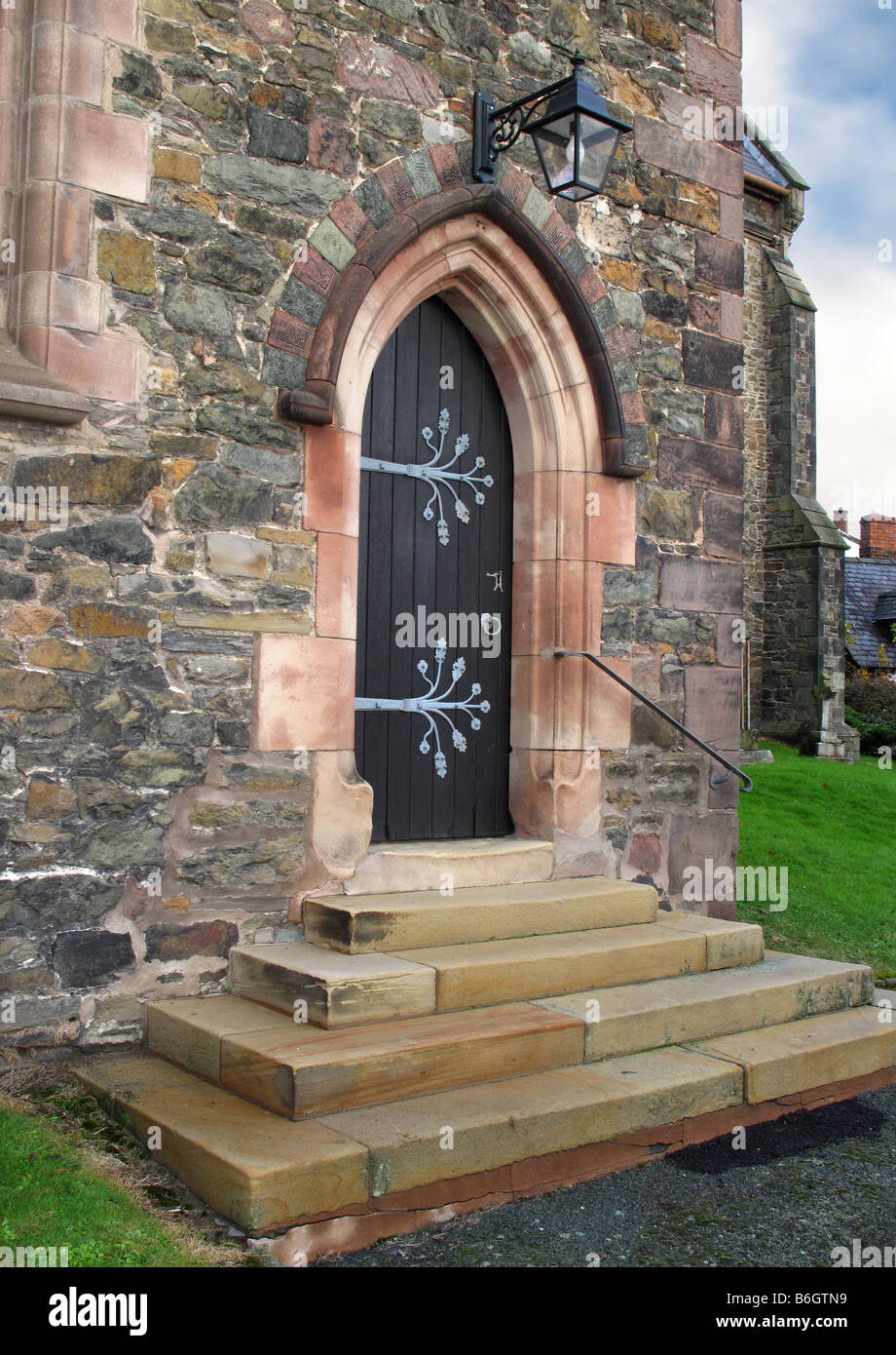 Chiesa di pietra portale ad arco con porta di legno ornato di lamiera cerniere, gradini in pietra e ghisa lanterna sopra. Foto Stock