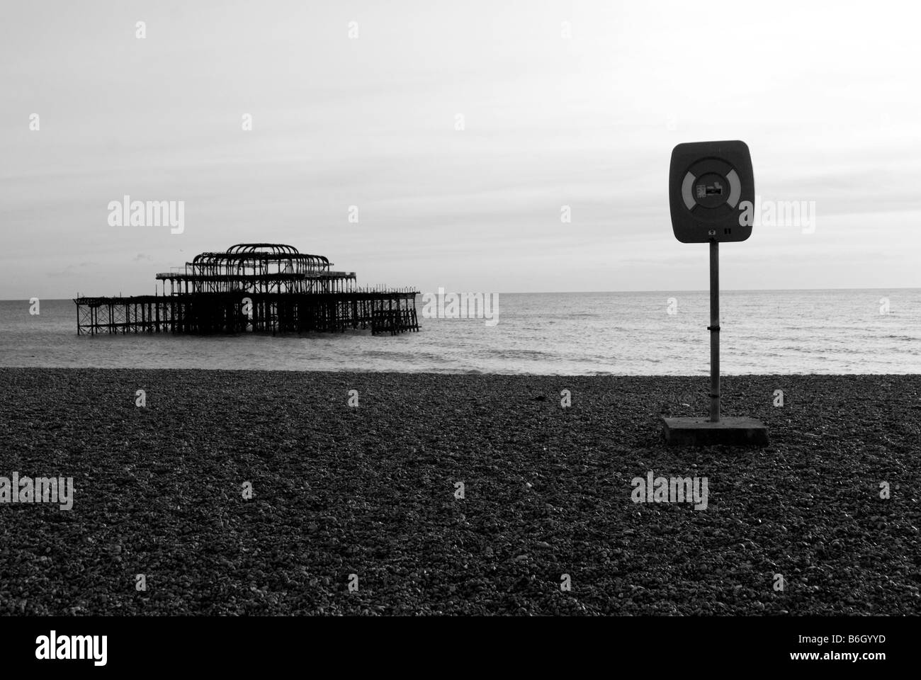 Una immagine di una vita anello di salvataggio con i resti di Brightons Molo Ovest in background su una tranquilla giornata sulla spiaggia Foto Stock