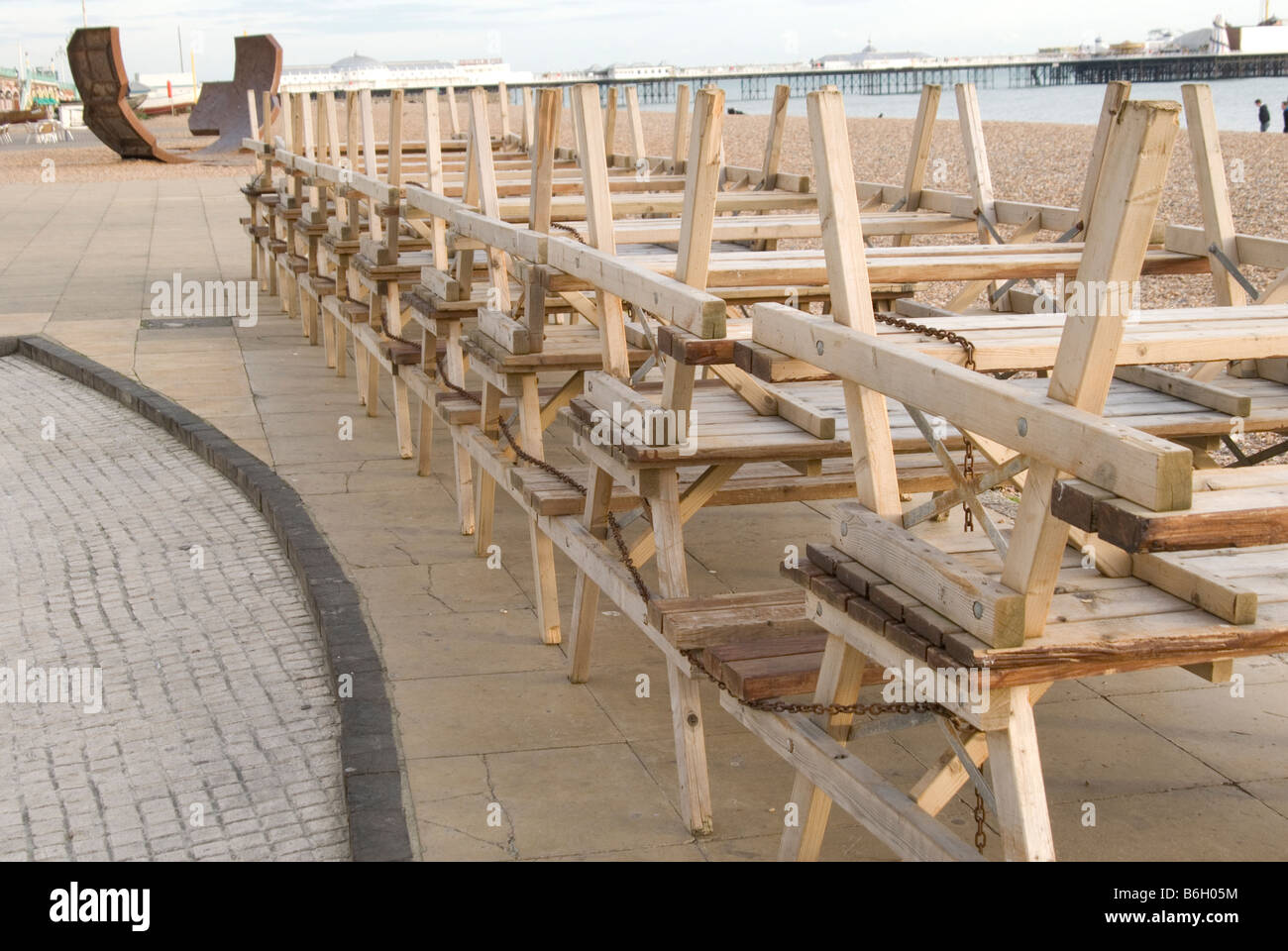 Panche allineate e impilati su Brighton Sea Front, una scultura, la spiaggia e il molo di Brighton può essere visto in background Foto Stock