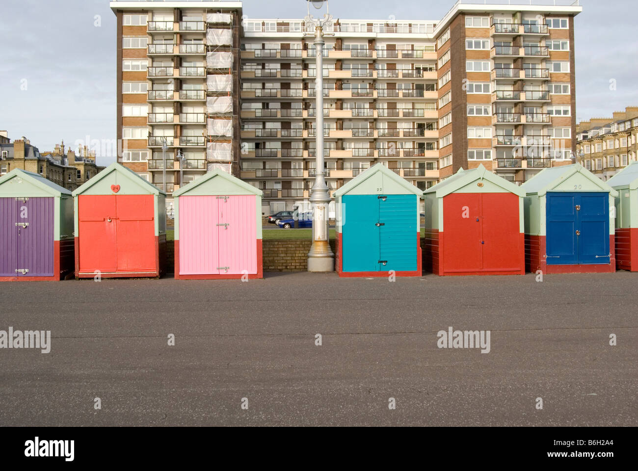 Una immagine della pittoresca spiaggia di capanne in Brighton con un blocco di appartamenti in background e una lampada posta tra la spiaggia di capanne. Foto Stock