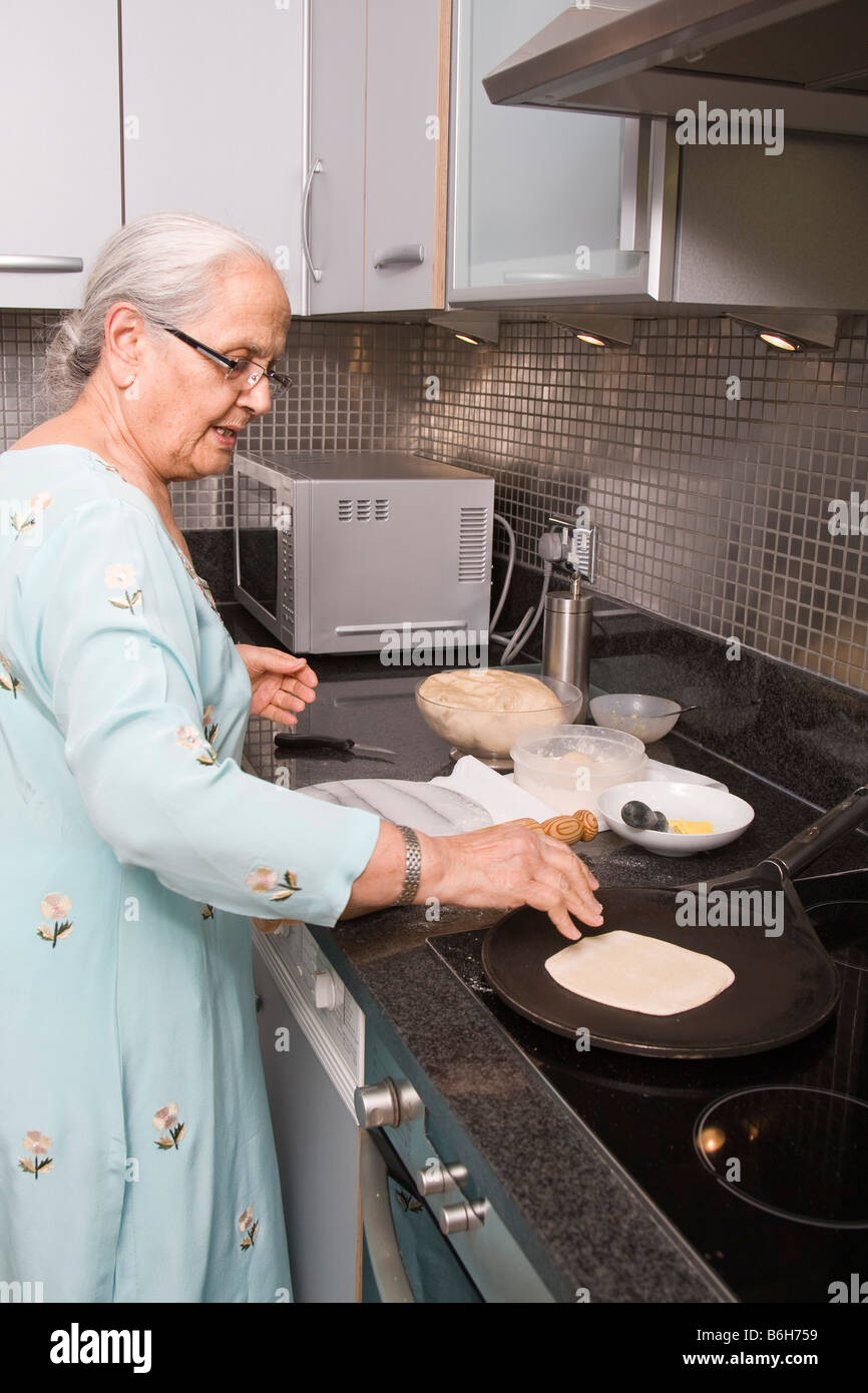 Senior donna indiana indossando Sari e Chapatis cottura nella cucina moderna Foto Stock