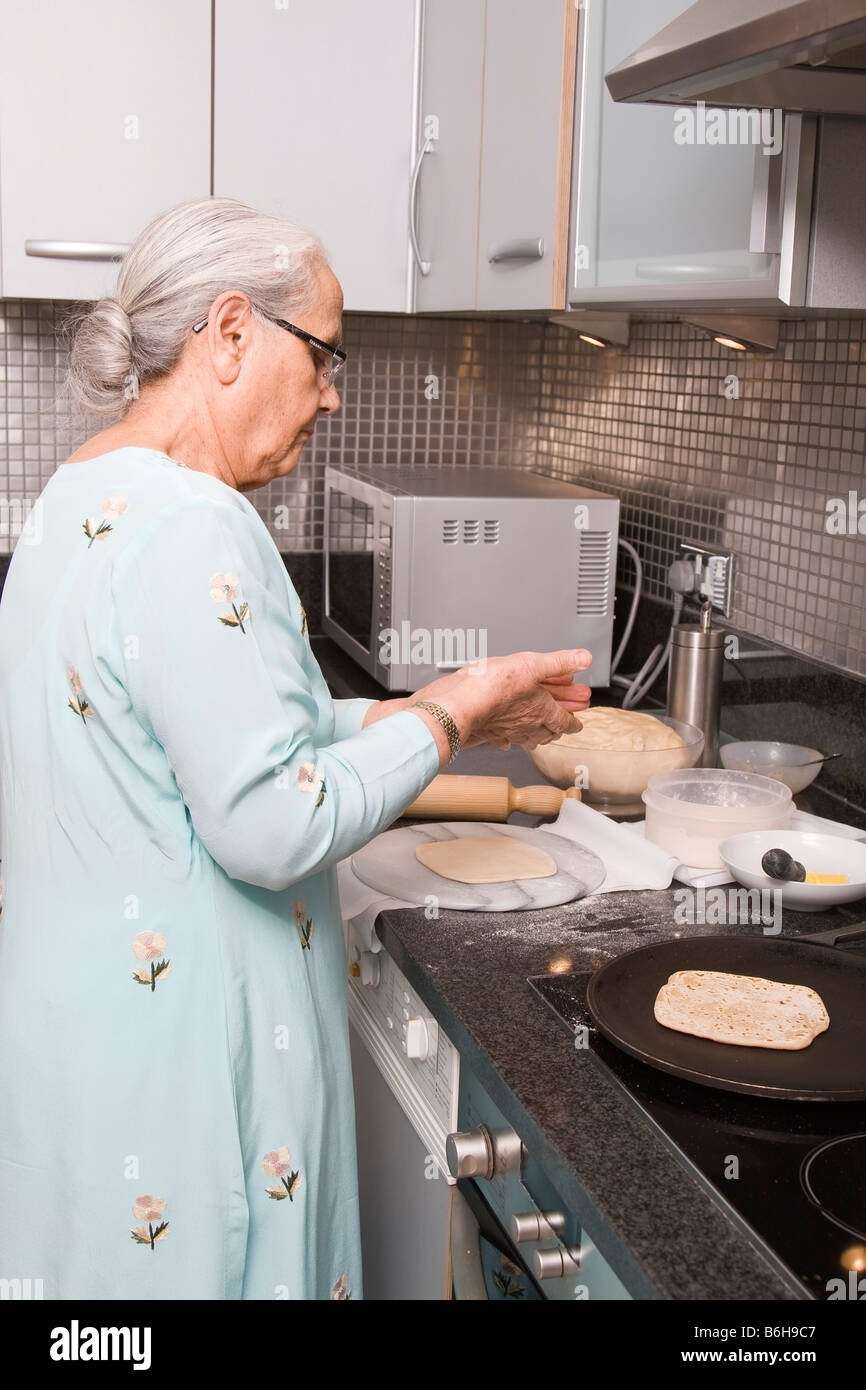 Senior donna indiana indossando Sari e Chapatis cottura nella cucina moderna Foto Stock