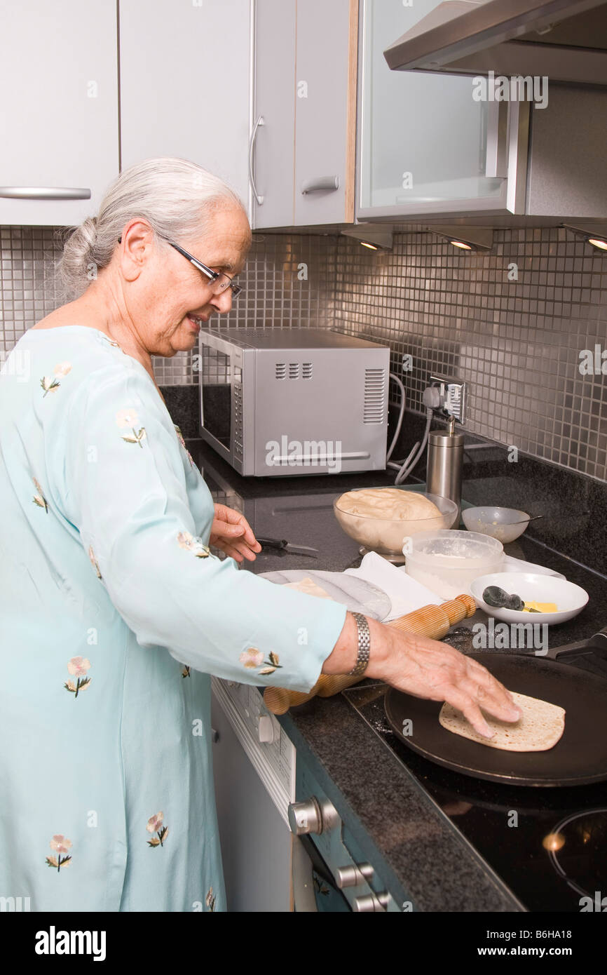 Senior donna indiana indossando Sari e Chapatis cottura nella cucina moderna Foto Stock