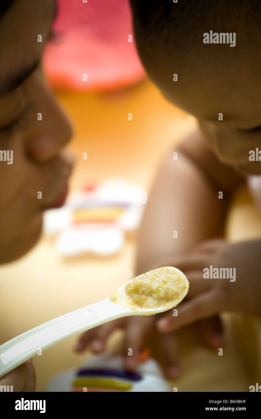 Etnia asiatica giovane madre sana alimentazione Porridge al suo bambino Foto Stock