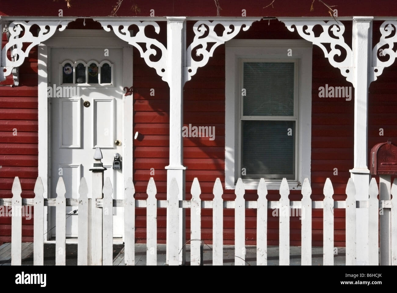 Chiudere la vista, parte anteriore portico di casa vittoriana con red clapboard schierata, verniciato bianco porta di ingresso, traforature & Picket Fence Foto Stock