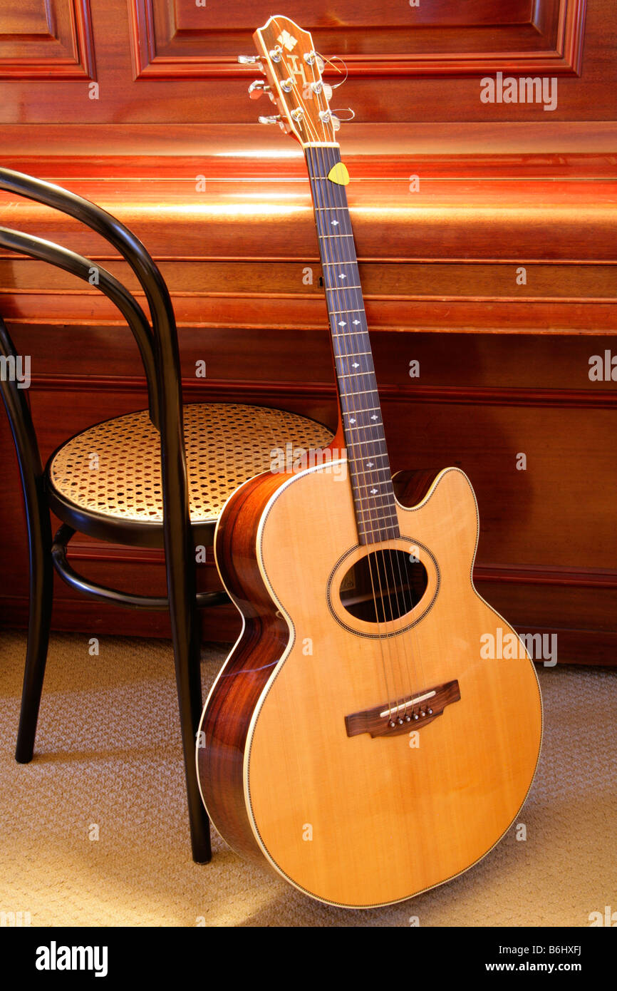 Progettato individualmente flat top chitarra acustica con suono ovale foro e proprietari monogram intarsiata contro la sedia chiusa e pianoforte. Foto Stock