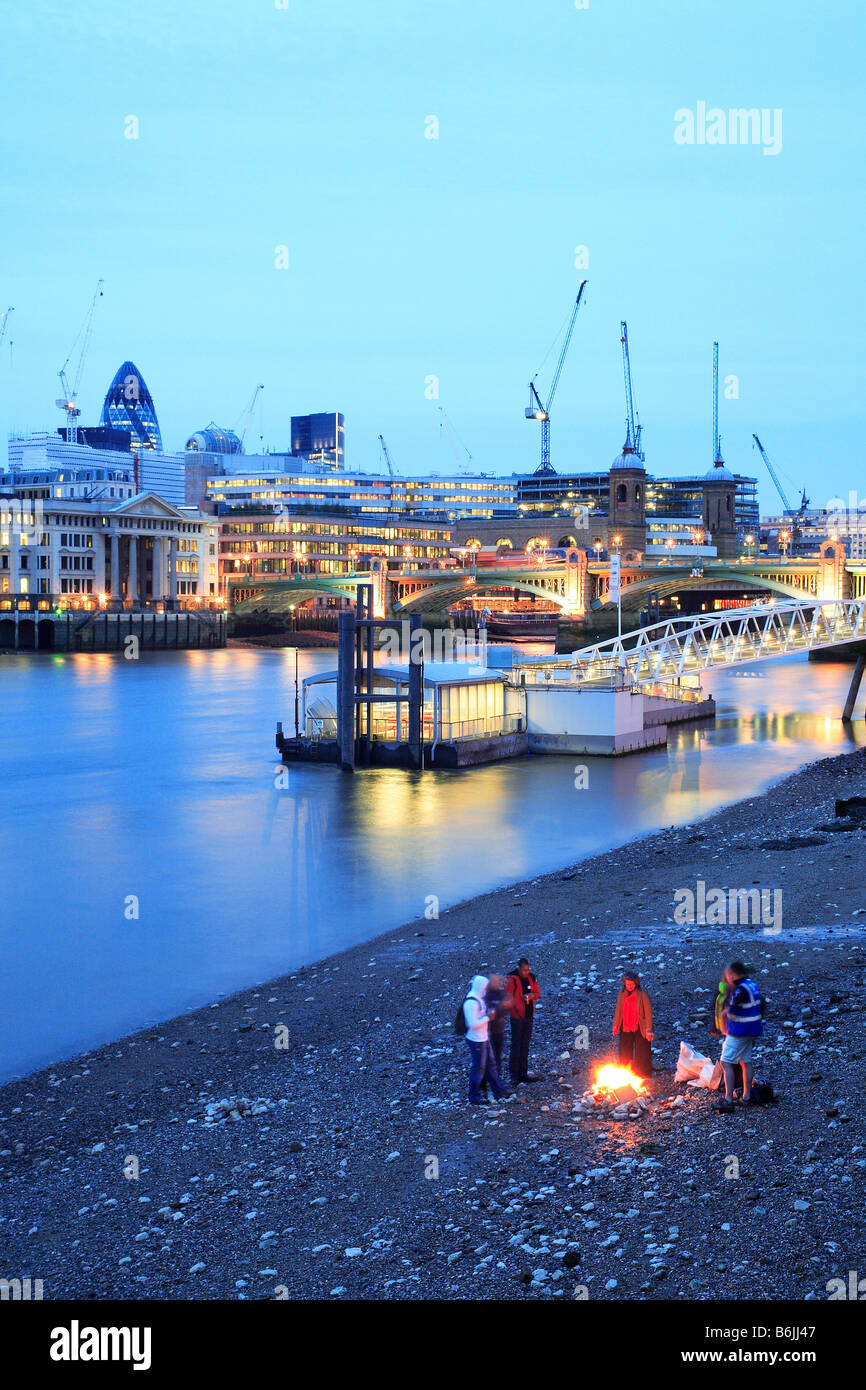 Le persone intorno al fuoco sul fiume Tamigi la spiaggia e il centro città di Londra di sera Foto Stock