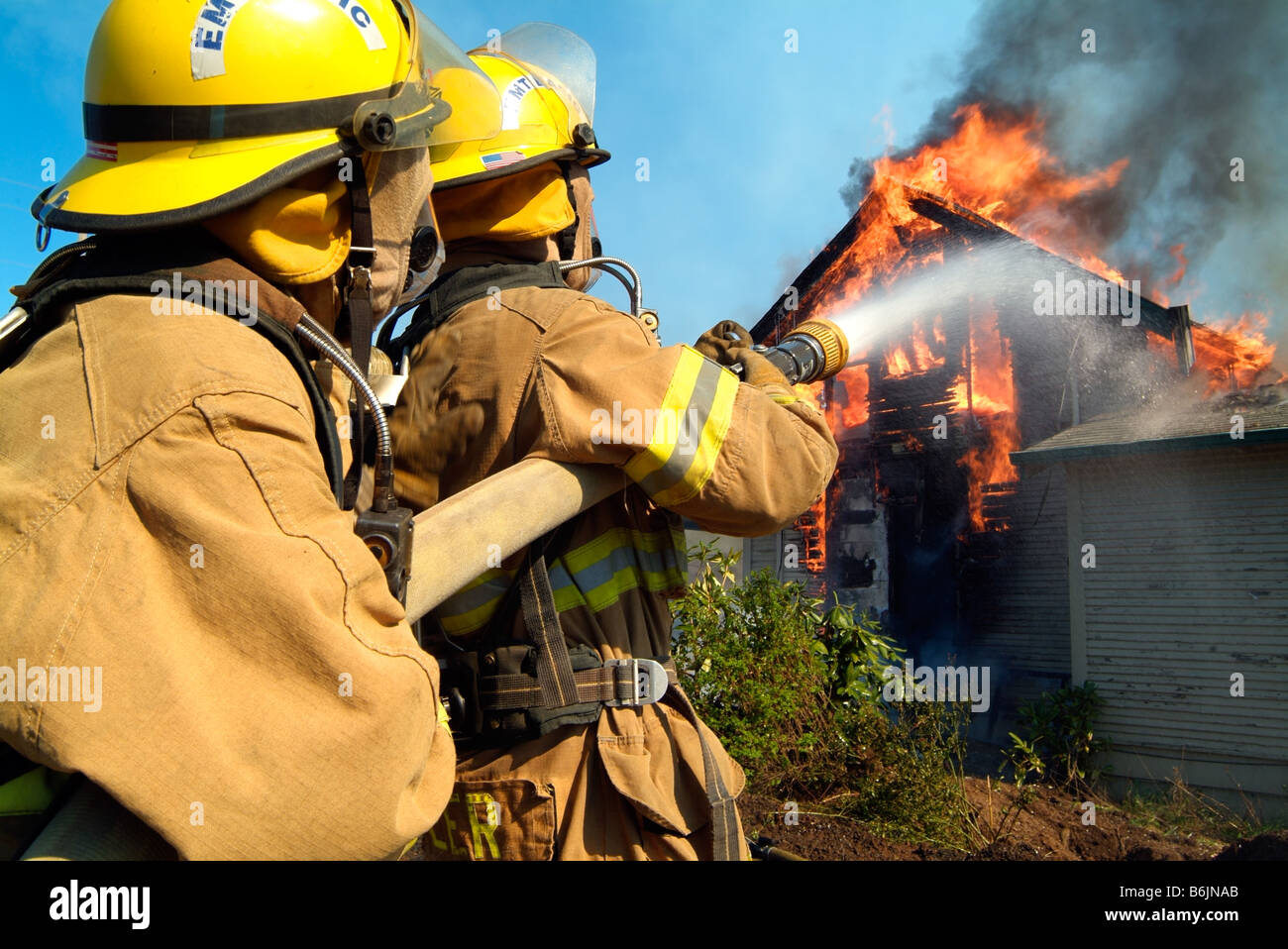 Due vigili del fuoco versare l'acqua su un inferno, il tentativo di abbattere le fiamme che stanno consumando una casa. Foto Stock