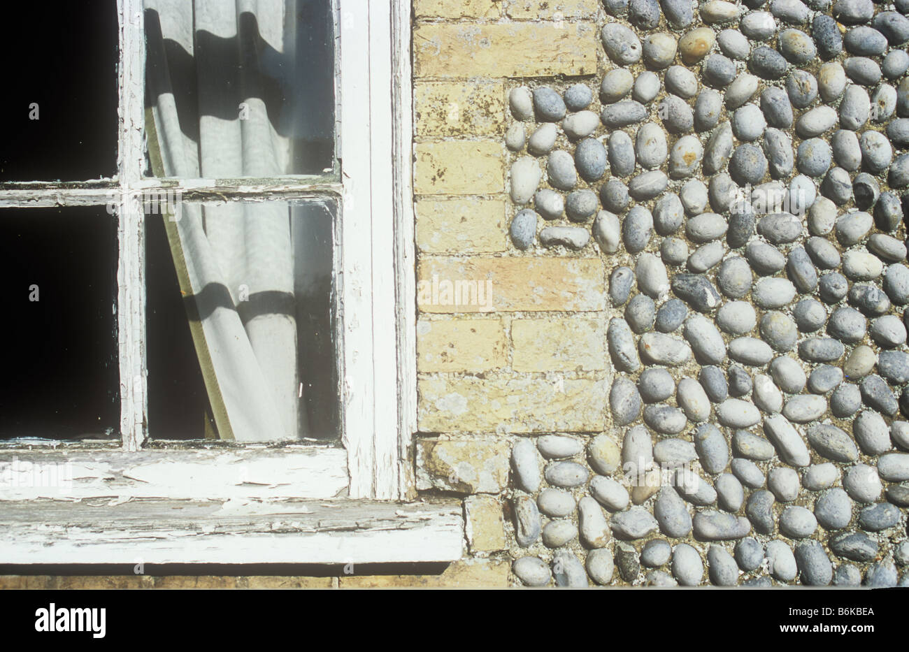 Dettaglio del telaio della finestra con tenda e ombra e incrinato la vernice bianca con un pallido mattone impostare surround in ordinate la parete di pietra focaia Foto Stock