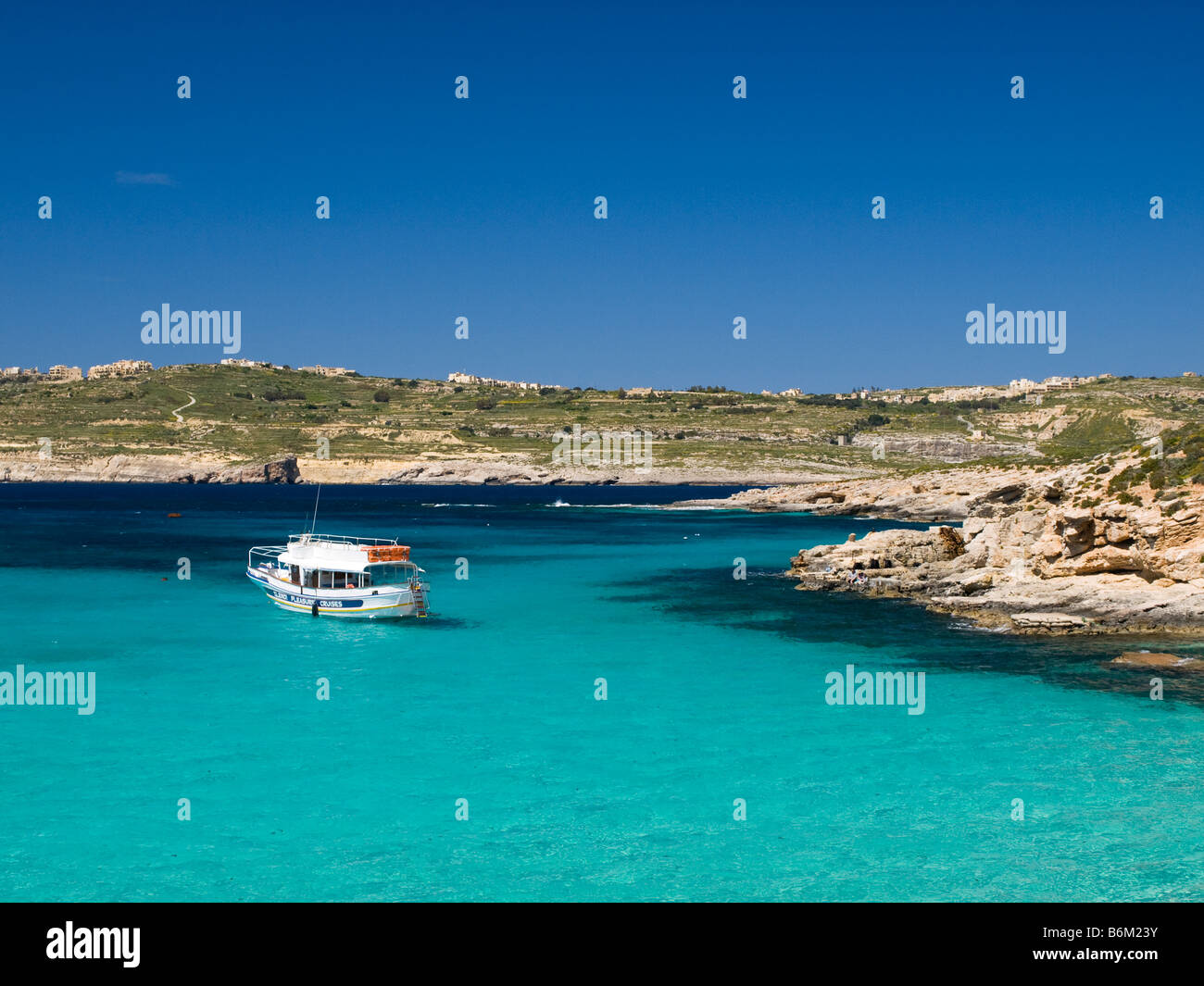 Una solitaria barca è ormeggiata in laguna blu. A Comino e Malta. Una vista dell'isola di Gozo è in distanza. Foto Stock