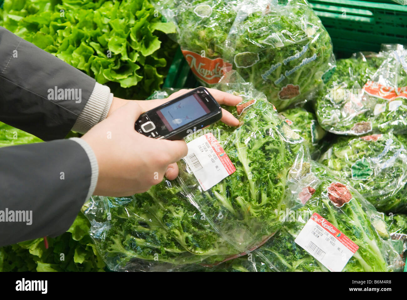 Giovane donna analizza il prezzo di un insalata confezionato nel suo telefono cellulare nel futuro reale di memorizzare una parte di Metro Group Foto Stock