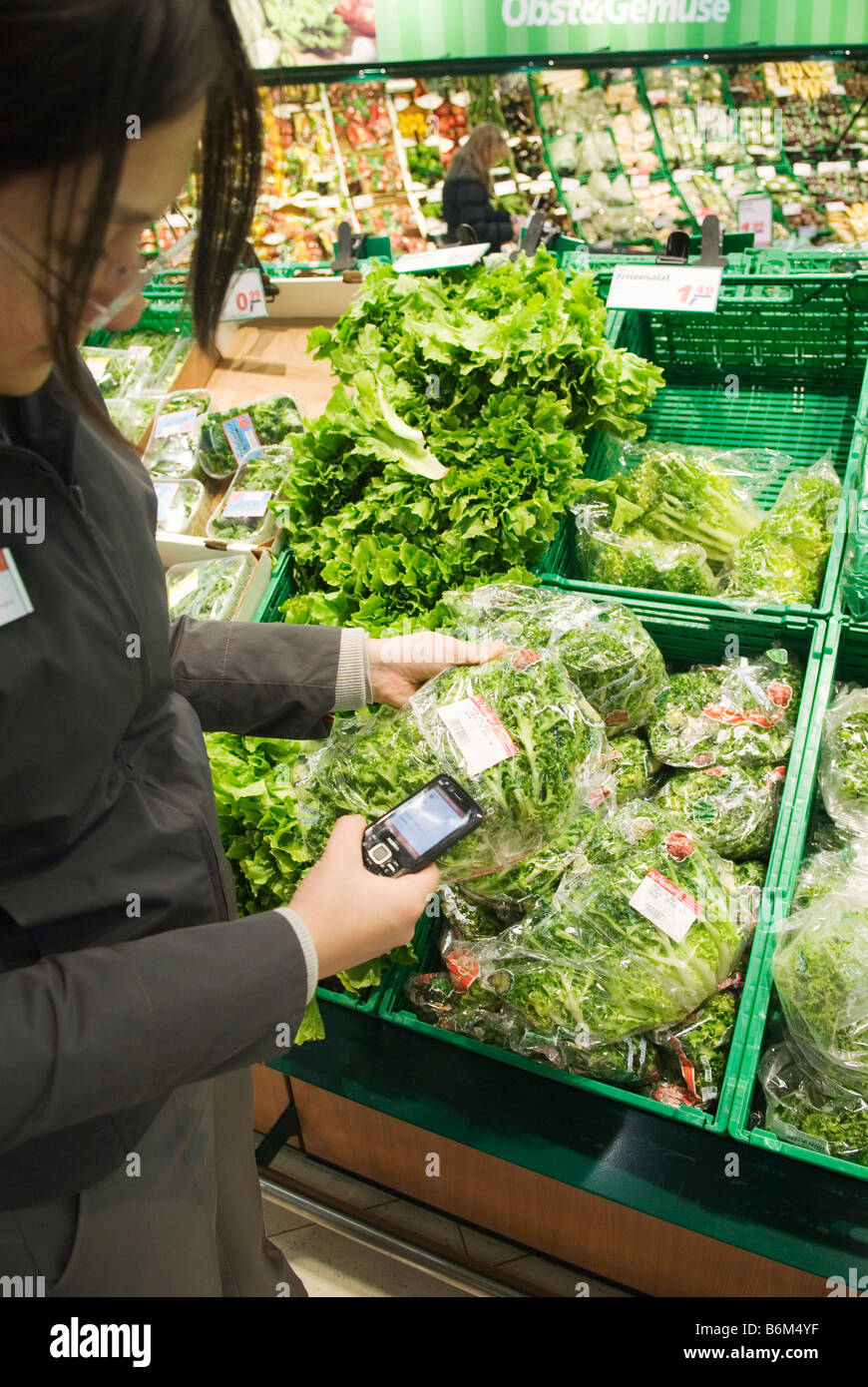 Giovane donna analizza il prezzo di un insalata confezionato nel suo telefono cellulare nel futuro reale di memorizzare una parte di Metro Group Foto Stock