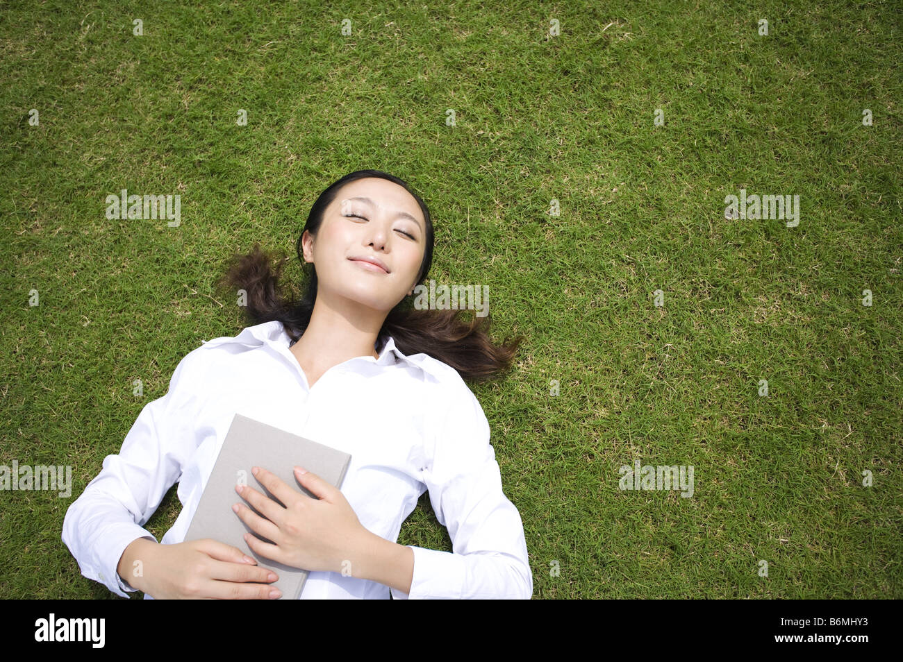 Giovane donna sonnecchiare sul prato azienda prenota Foto Stock