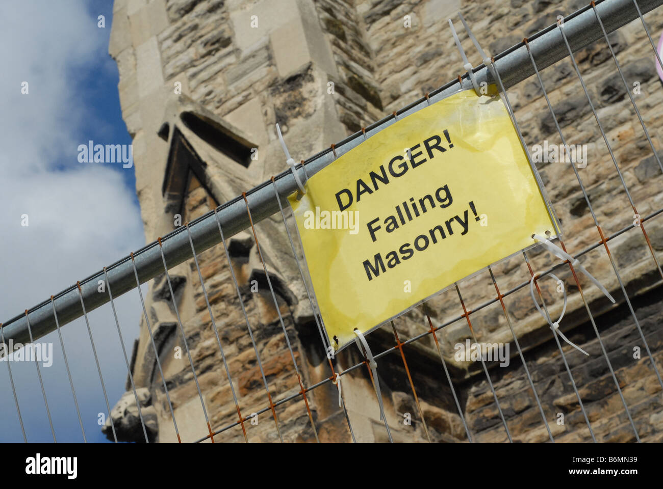Un segno su una catena collegamento recinto avvertimento circa la caduta di muratura nei pressi di una chiesa. Foto Stock