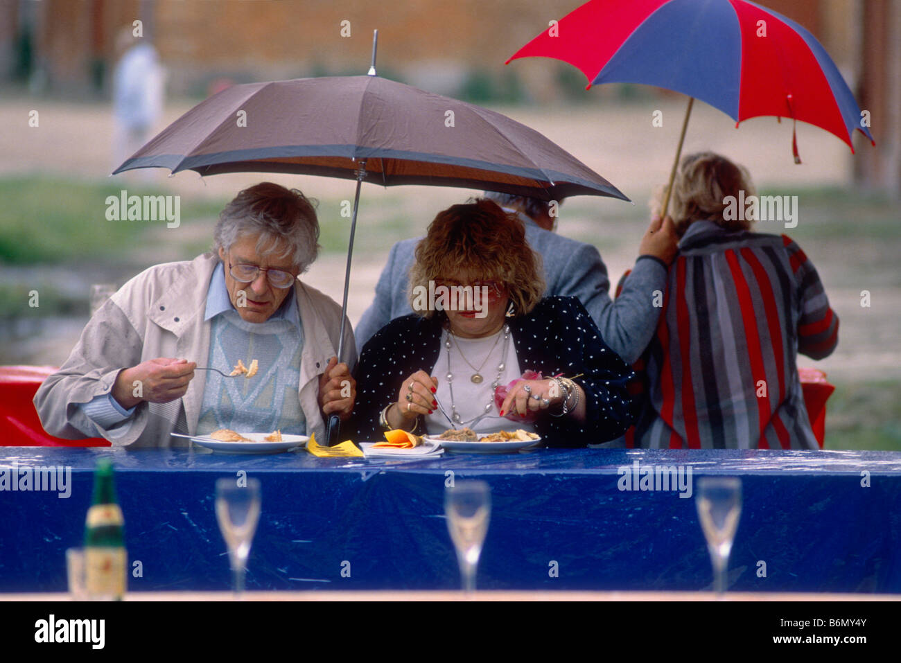 I visitatori di un concerto dal Schleswig-Holstein-Music-Festival mangiare mentre piove nella fattoria cantiere sotto un ombrello Foto Stock