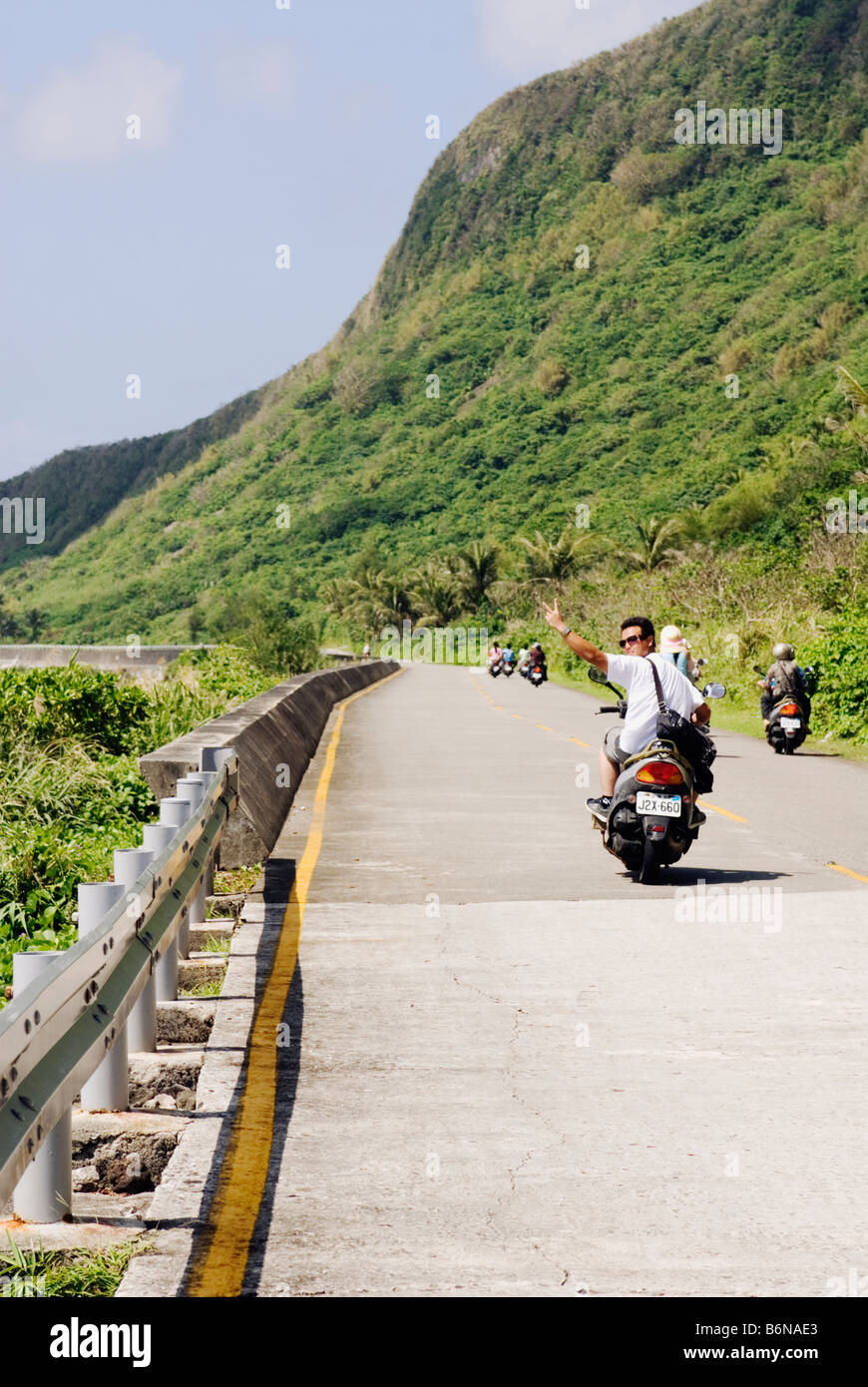 Taiwan, Isola Verde, giovane uomo alla guida di scooter e guardando indietro gesticolando un segno di pace Foto Stock