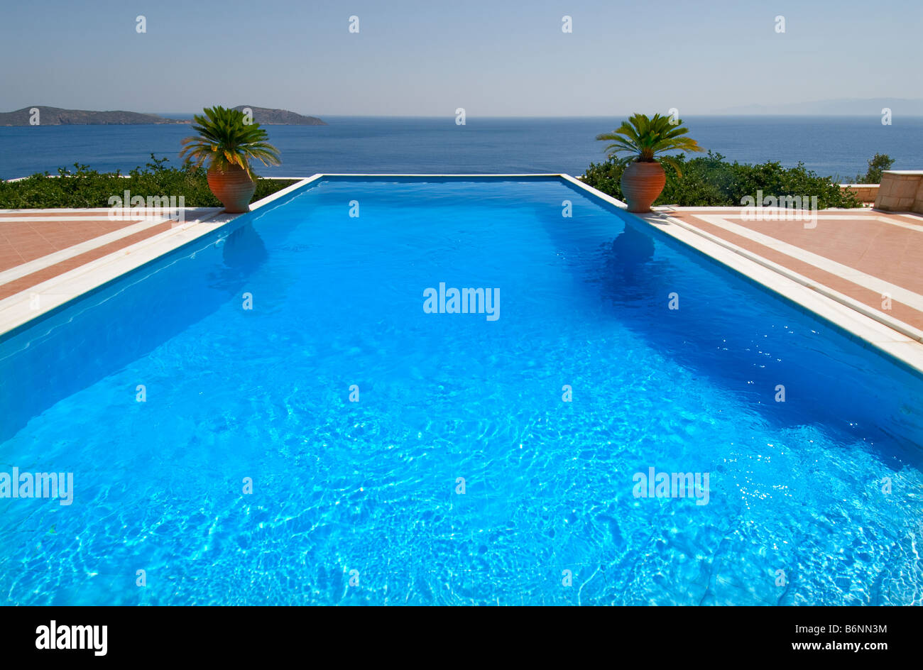 Esclusiva di lusso piscina infinity privata invitante un tuffo, affacciato sul Mar Egeo con palme e tipici grecian URN Foto Stock