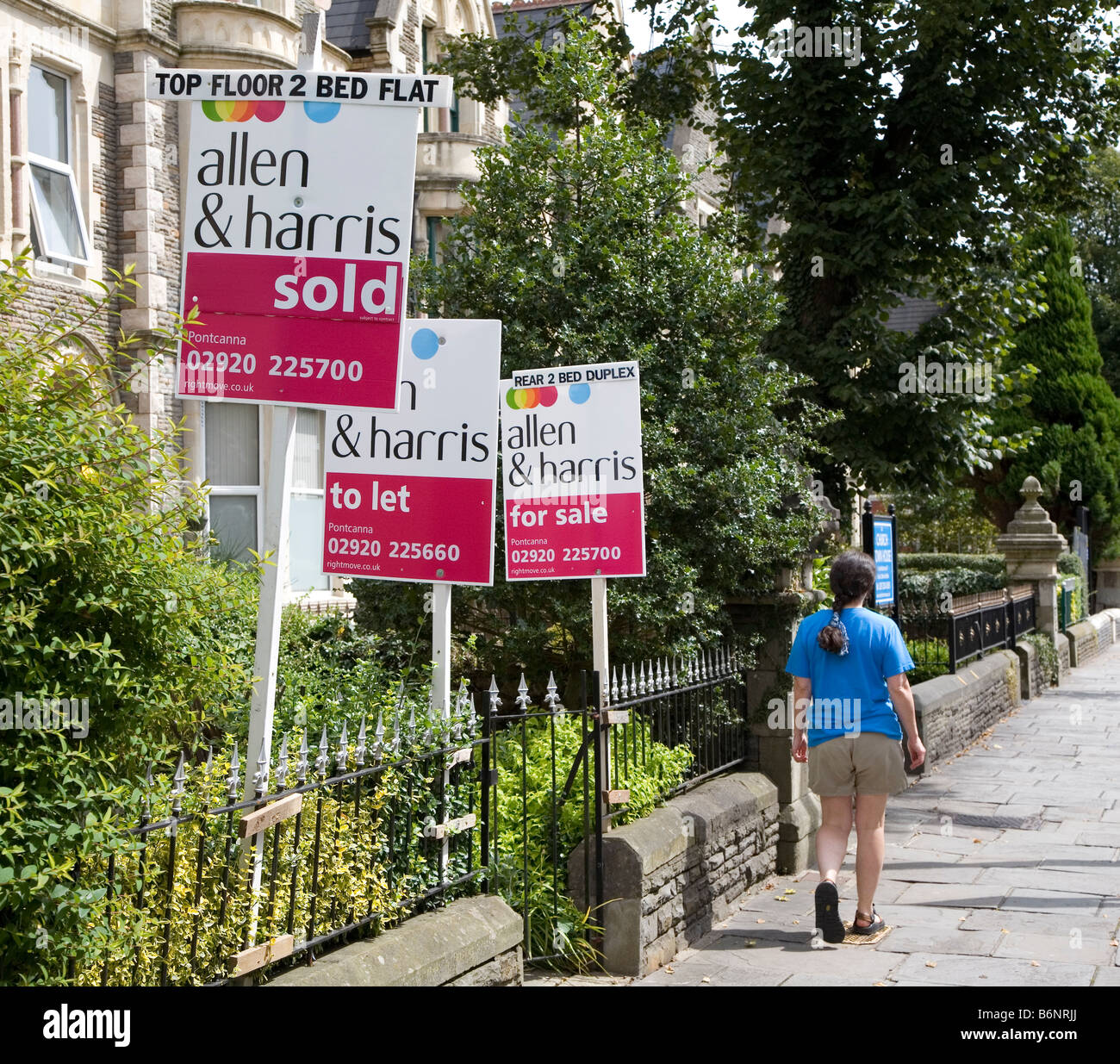 Donna oltrepassando tre in vendita casa segni con vendita venduto per lasciare Cardiff Wales UK Foto Stock