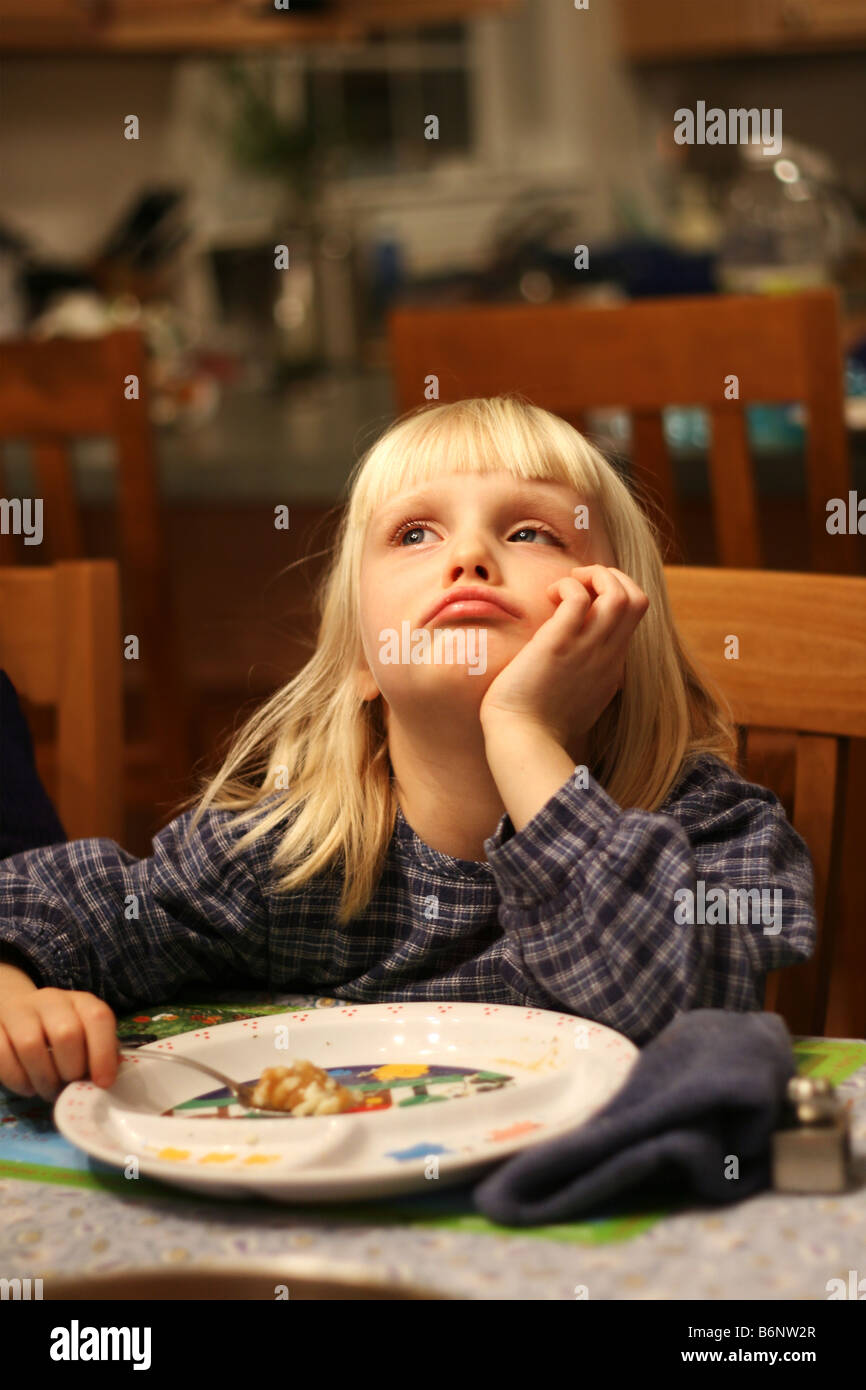 Un triste cinque anni ragazza bionda guardando verso l'alto ha un ultimo boccone della cena per mangiare Foto Stock